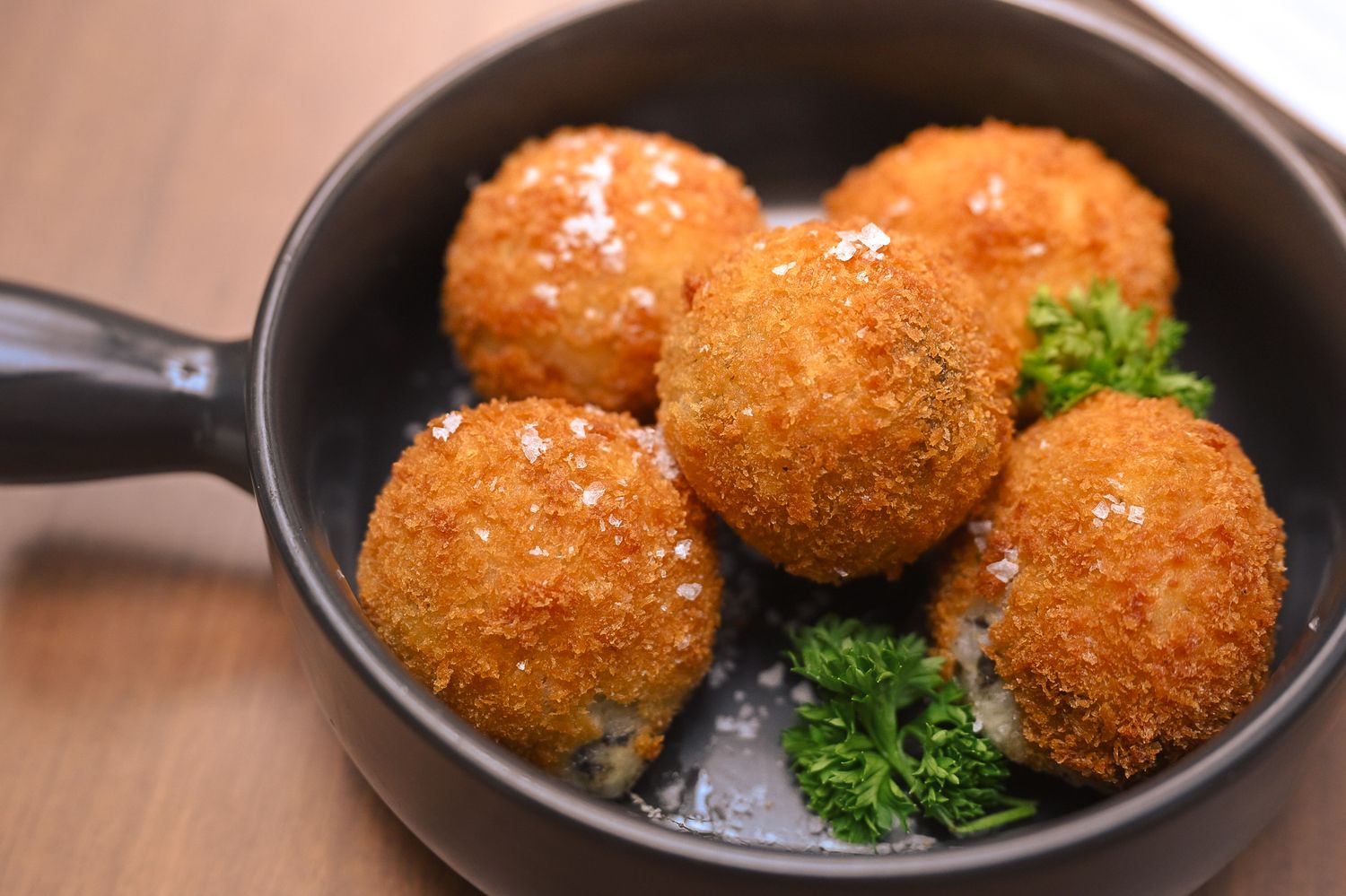 Golden brown crispy croquettes served with garnish in cast iron pan.