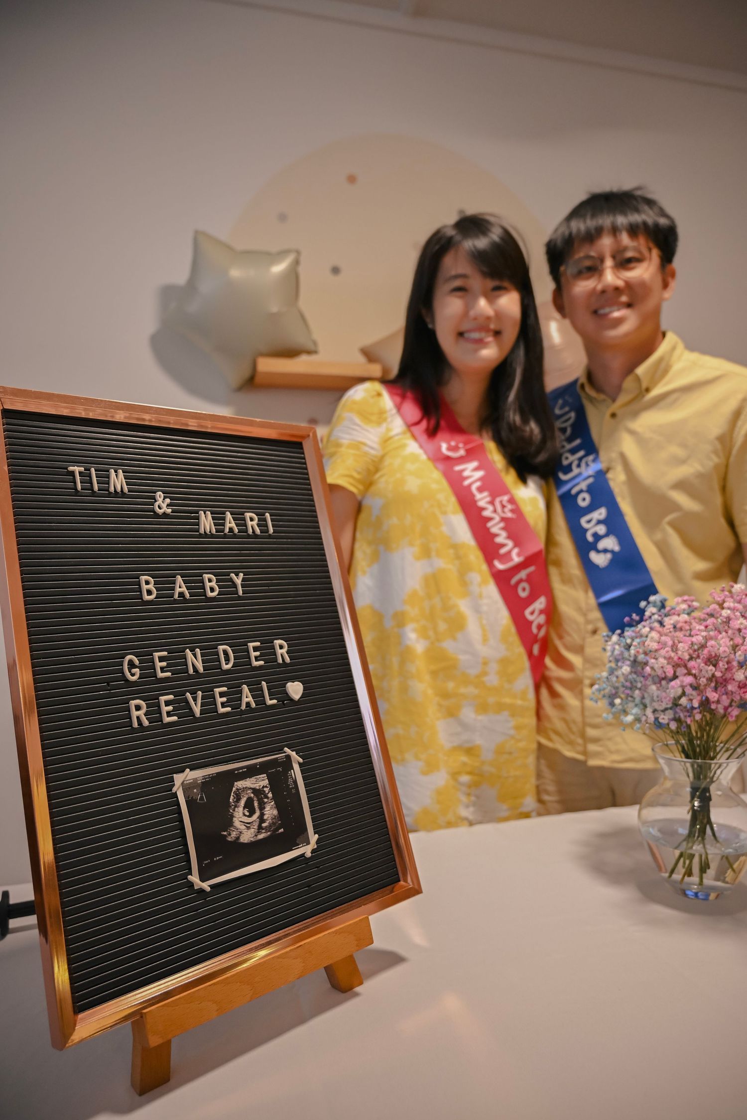 Letter board announcing a gender reveal party with decorative flowers and matching decor in the background.