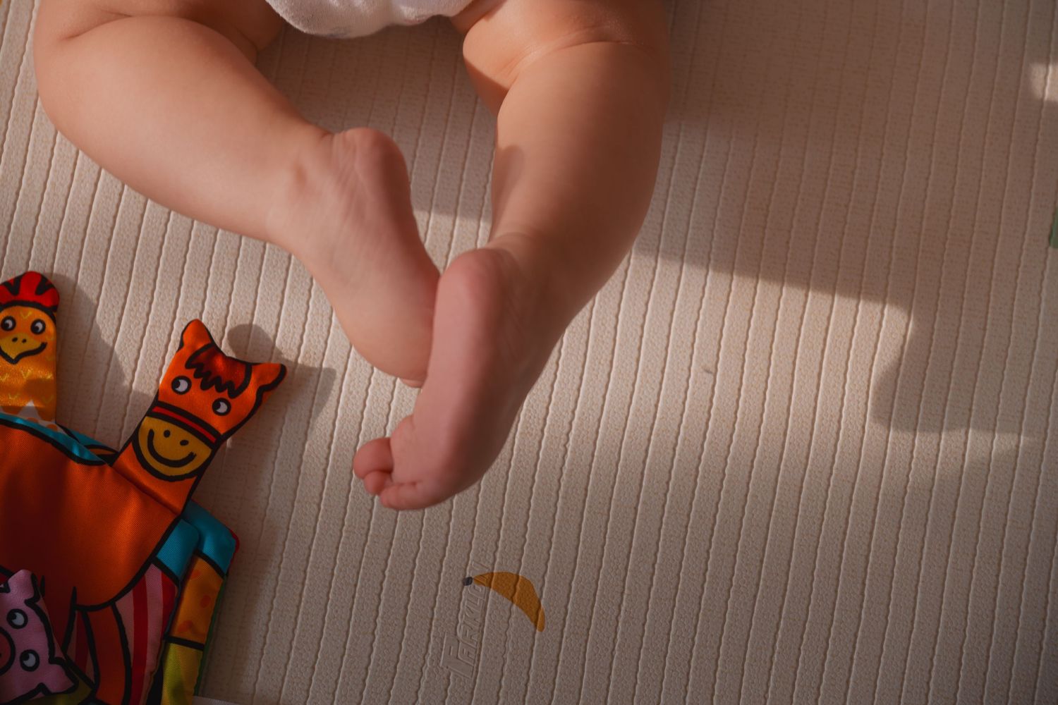 Close-up of baby feet resting on a striped mat next to colorful toy figures.