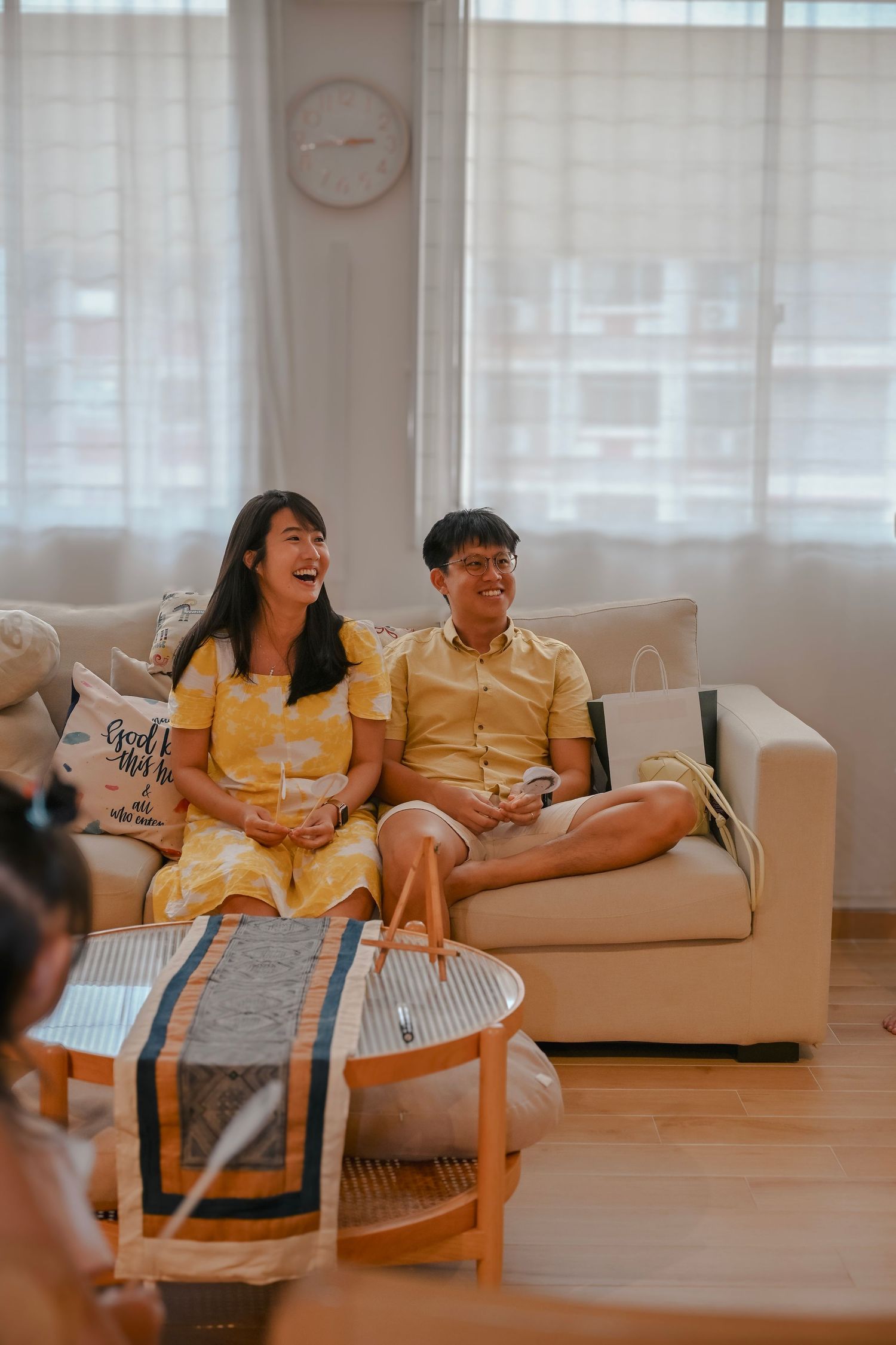 Bright living room scene with people relaxing on a white couch near large windows.