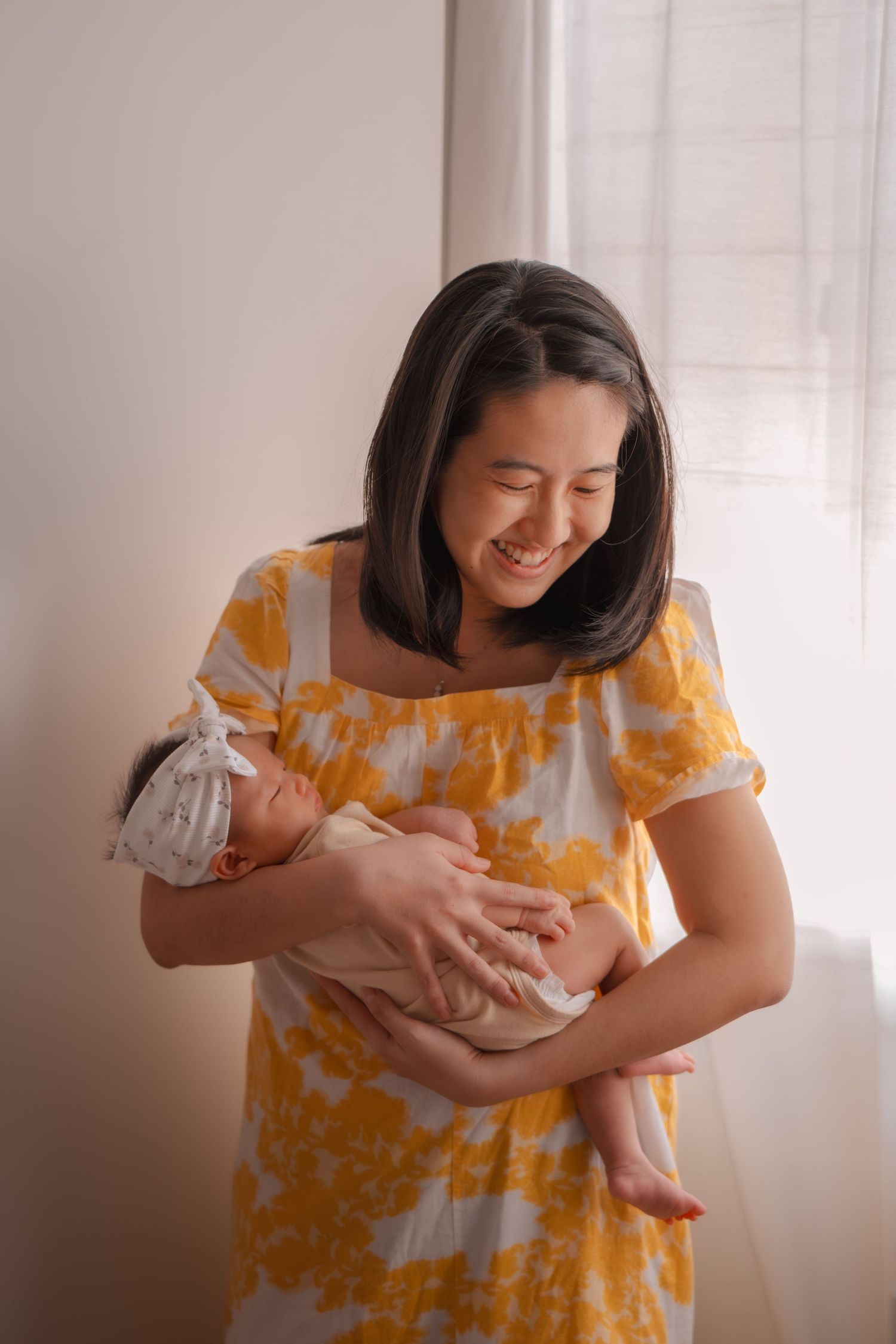 Woman in yellow floral dress holding and gazing lovingly at newborn baby.