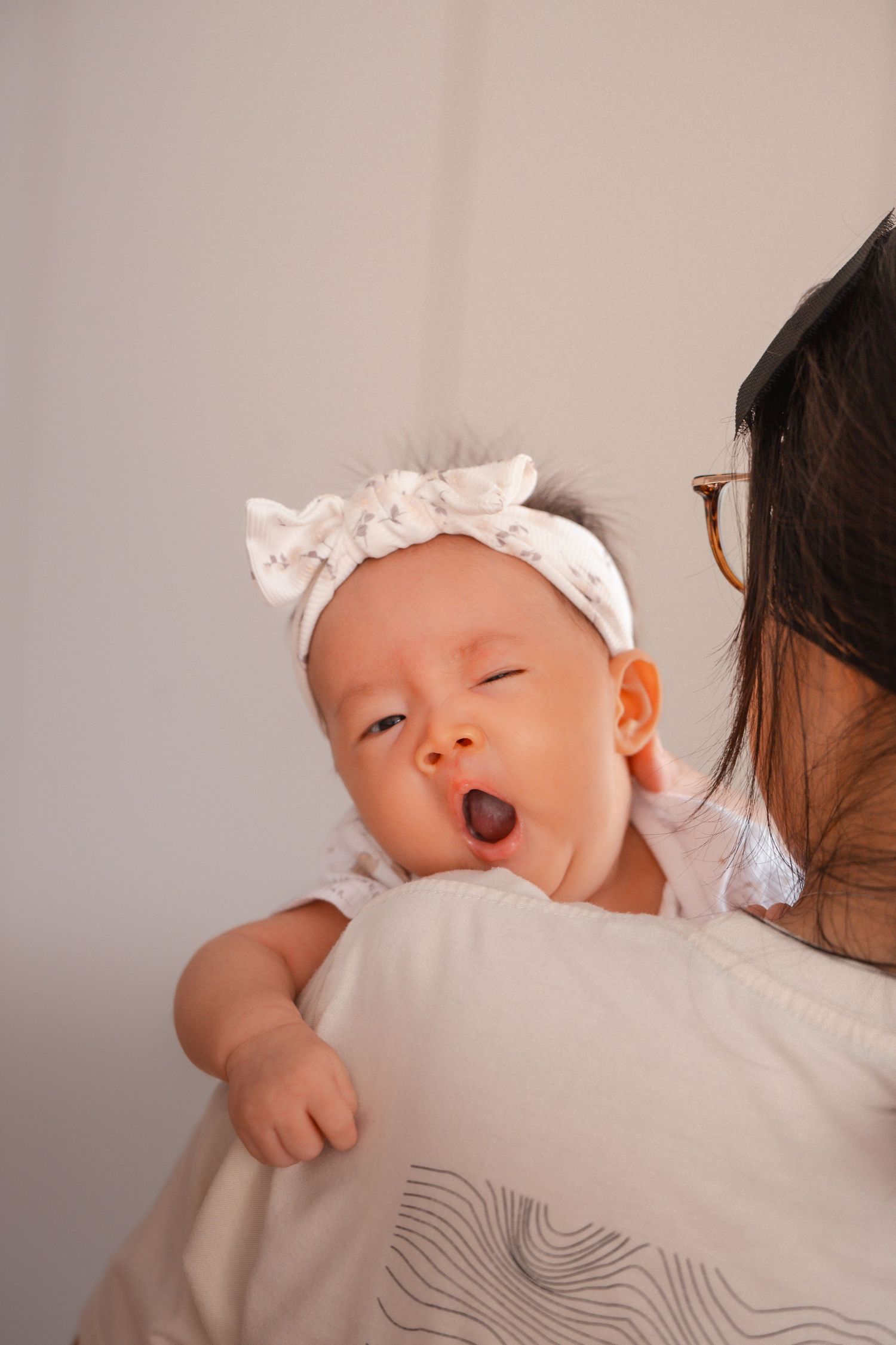 A sleeping newborn baby rests peacefully on someone's shoulder wearing a white cap.