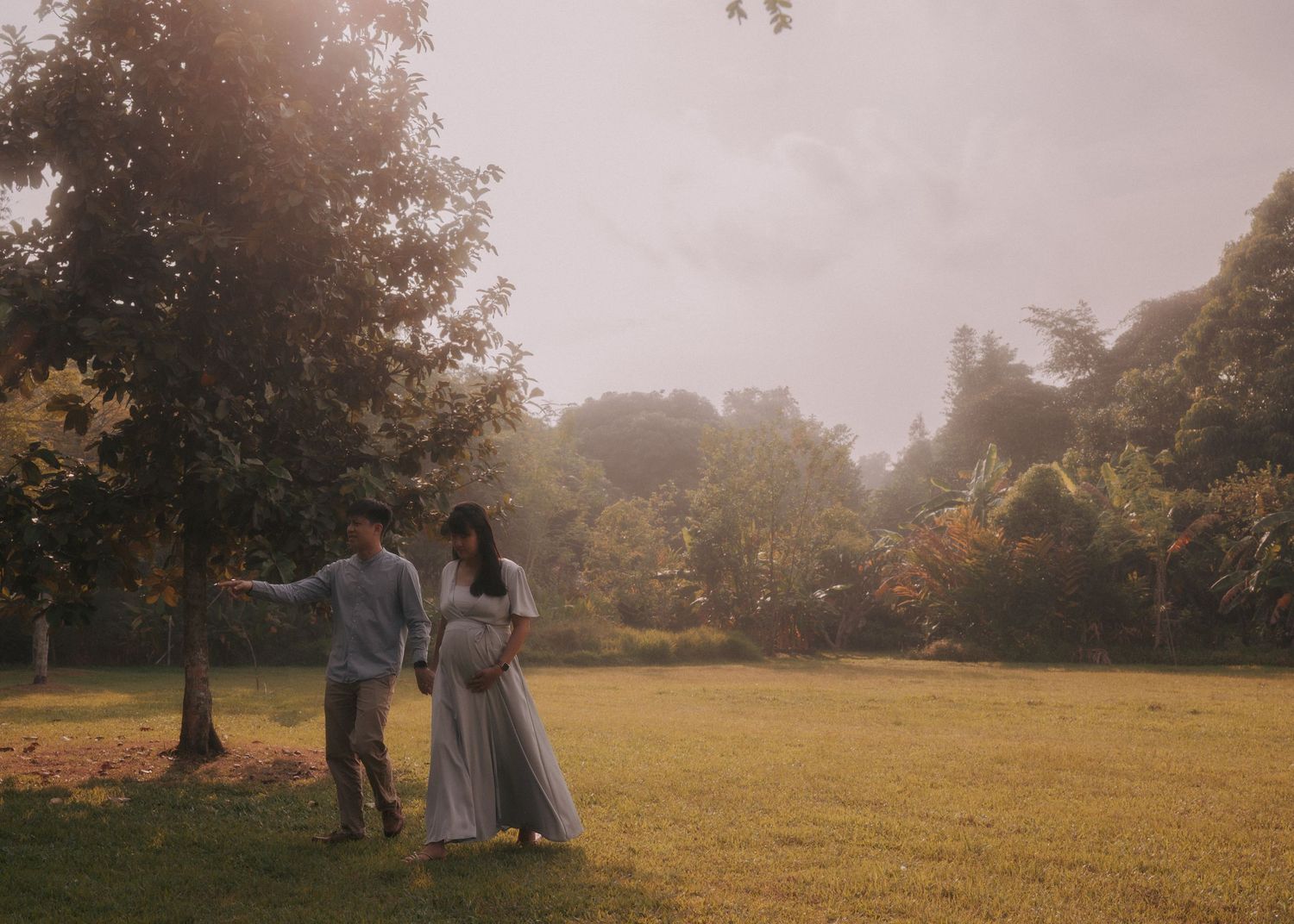 A couple walks hand in hand across a sunlit meadow during golden hour.