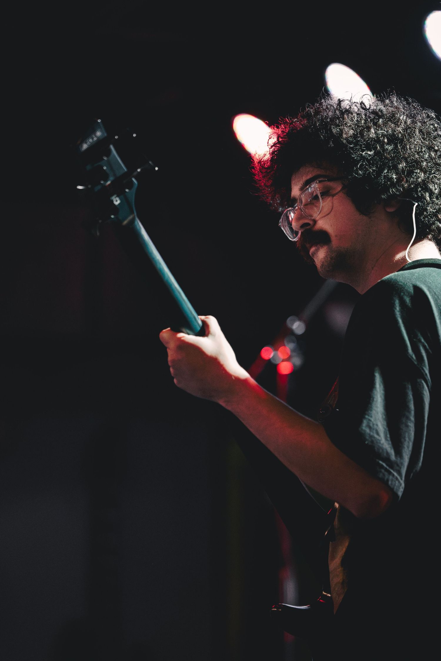 A silhouetted figure holds a guitar in a dark environment with red accent lighting.