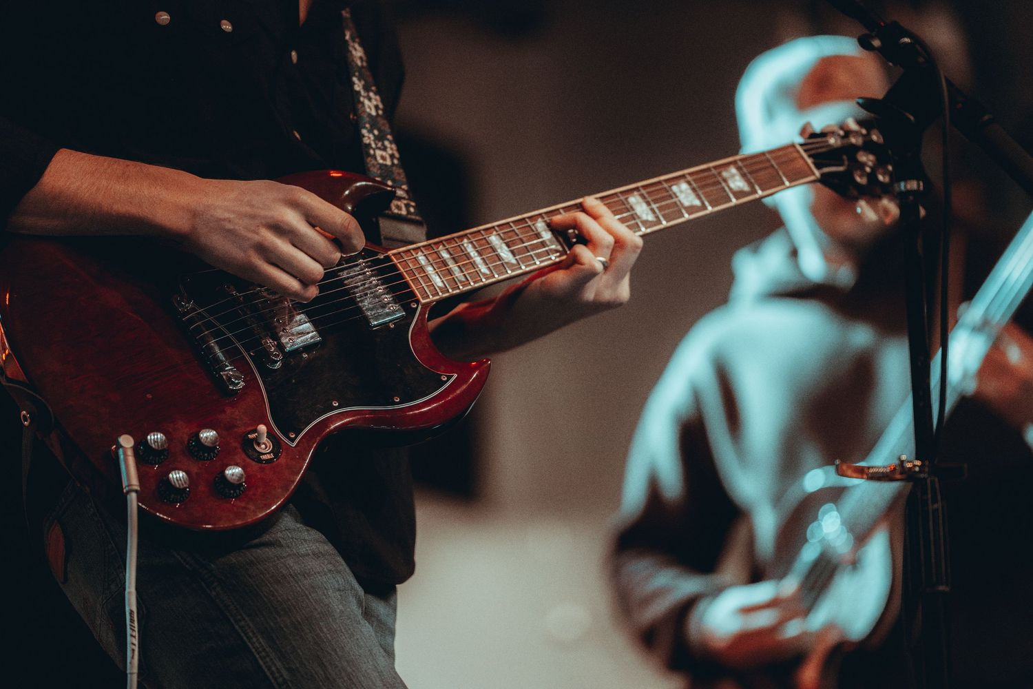 Musician playing a red Gibson SG electric guitar on stage during a live performance.
