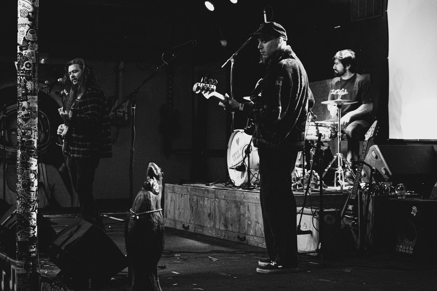 Black and white photo of a live band performing on stage with guitars and drums in a dark venue.