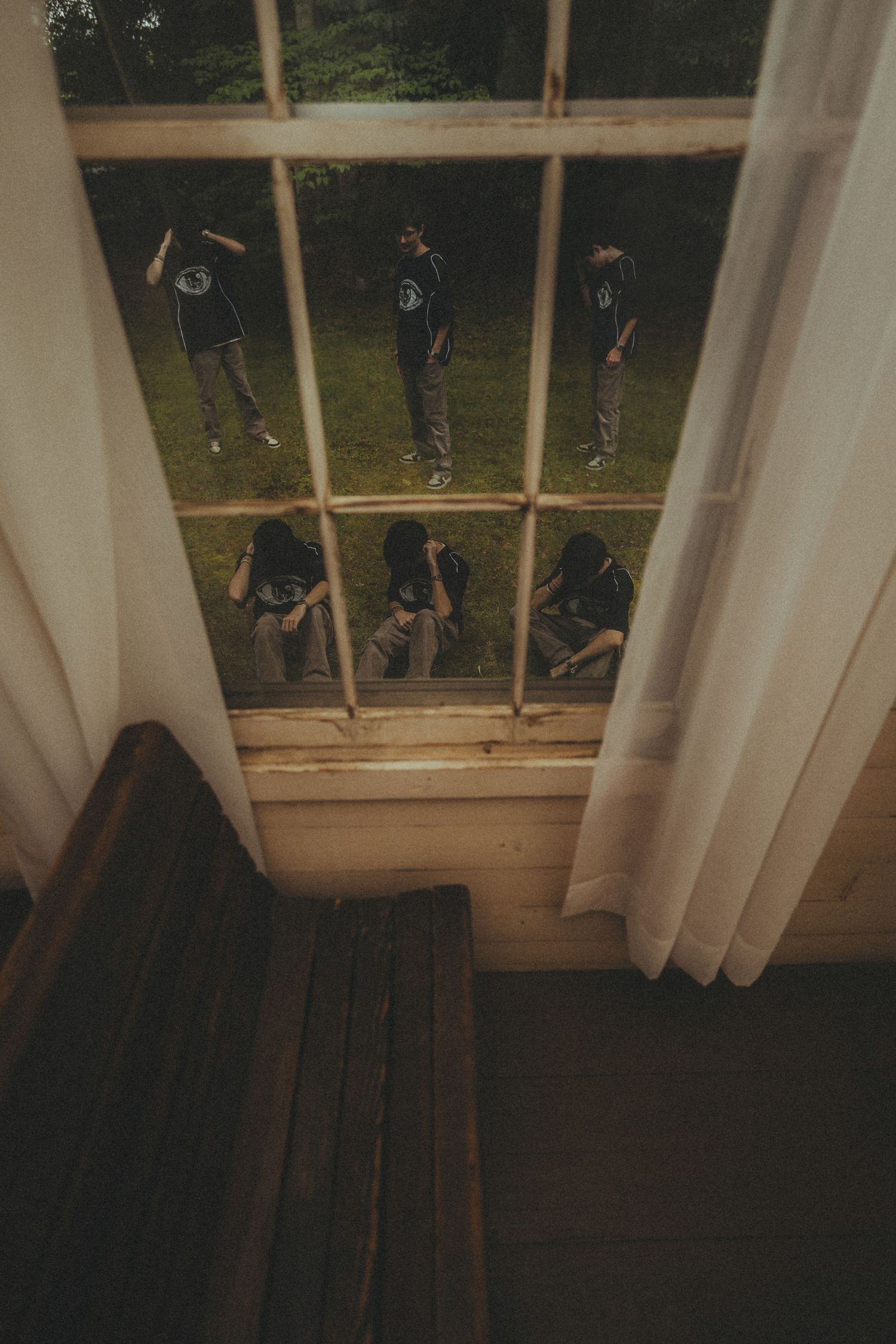 Group of young people in matching dark shirts seen through a window with curtains, viewed from interior staircase.