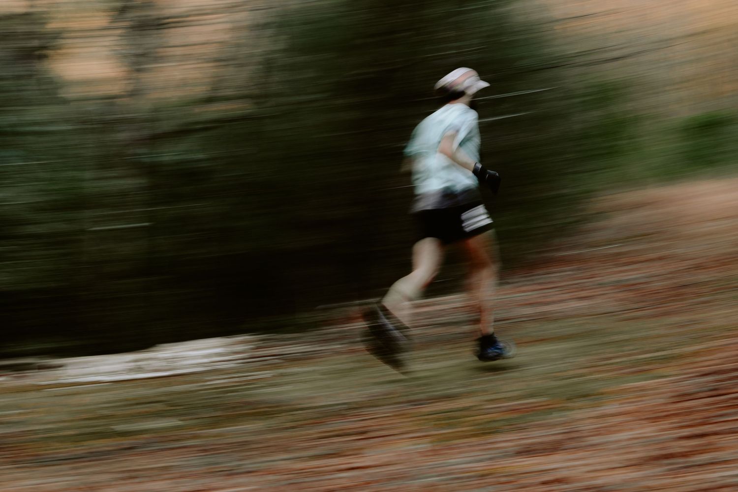 A person runs on a dirt trail through a wooded area in motion-blurred action sequence photography.