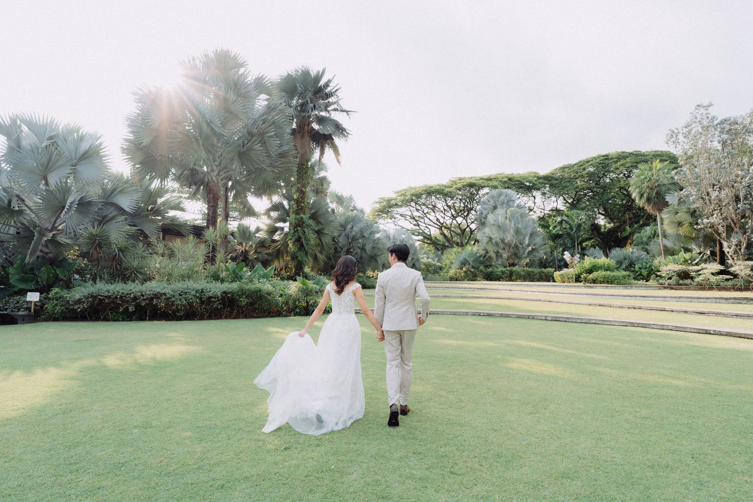A couple walks together on a lush green golf course during a sunny outdoor wedding celebration.