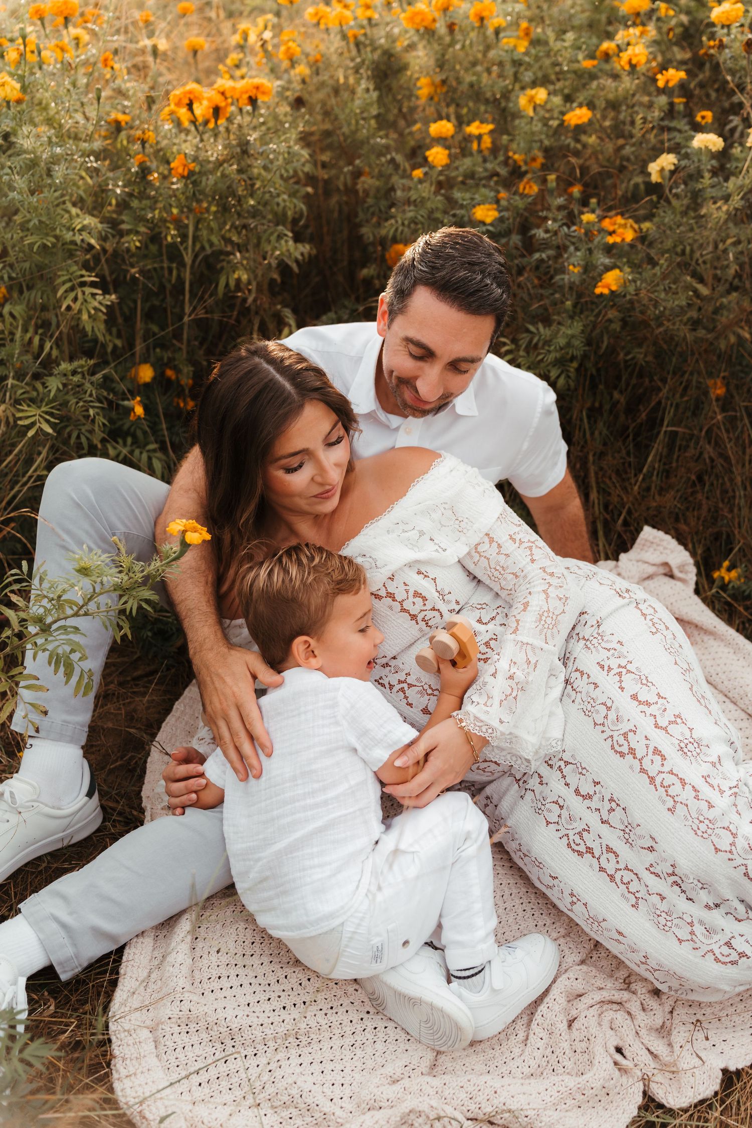 Pregnant mother being snuggled by son and husband in a field of marigolds near Charlotte, NC captured during a lifestyle maternity session.