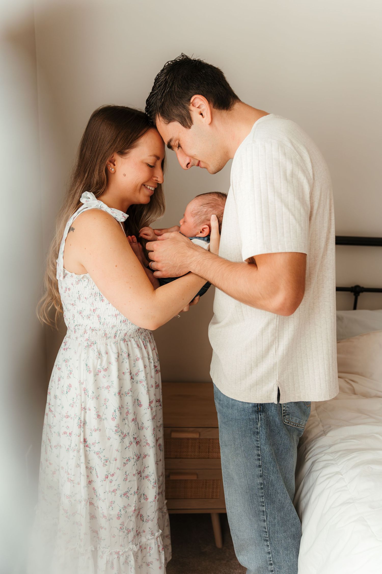 Parents holding their newborn baby boy near a bedroom window during a Charlotte, NC in-home newborn session.