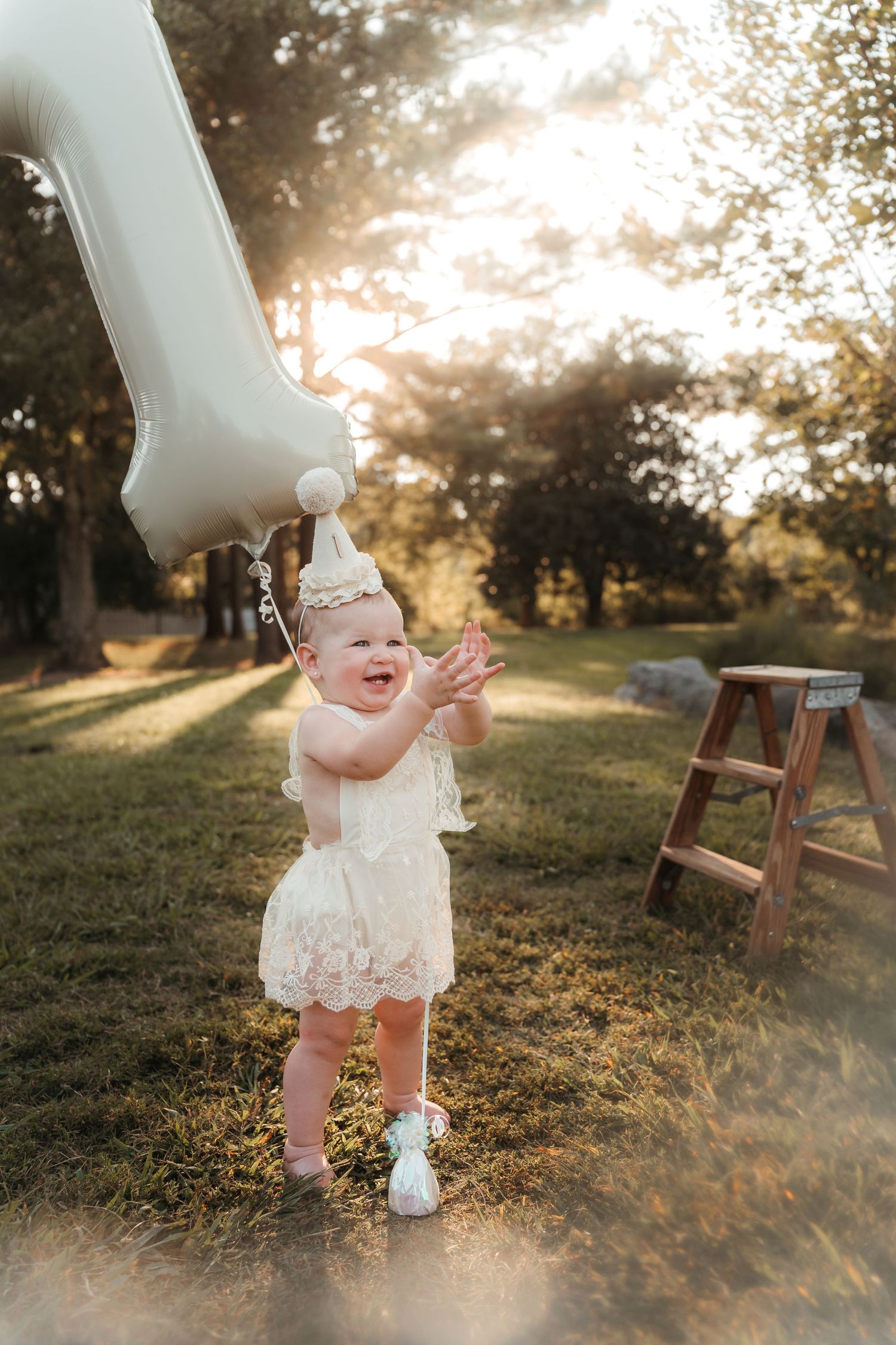 Child clapping hands with balloon celebrating first birthday during a Charlotte, NC cake smash session outdoors.