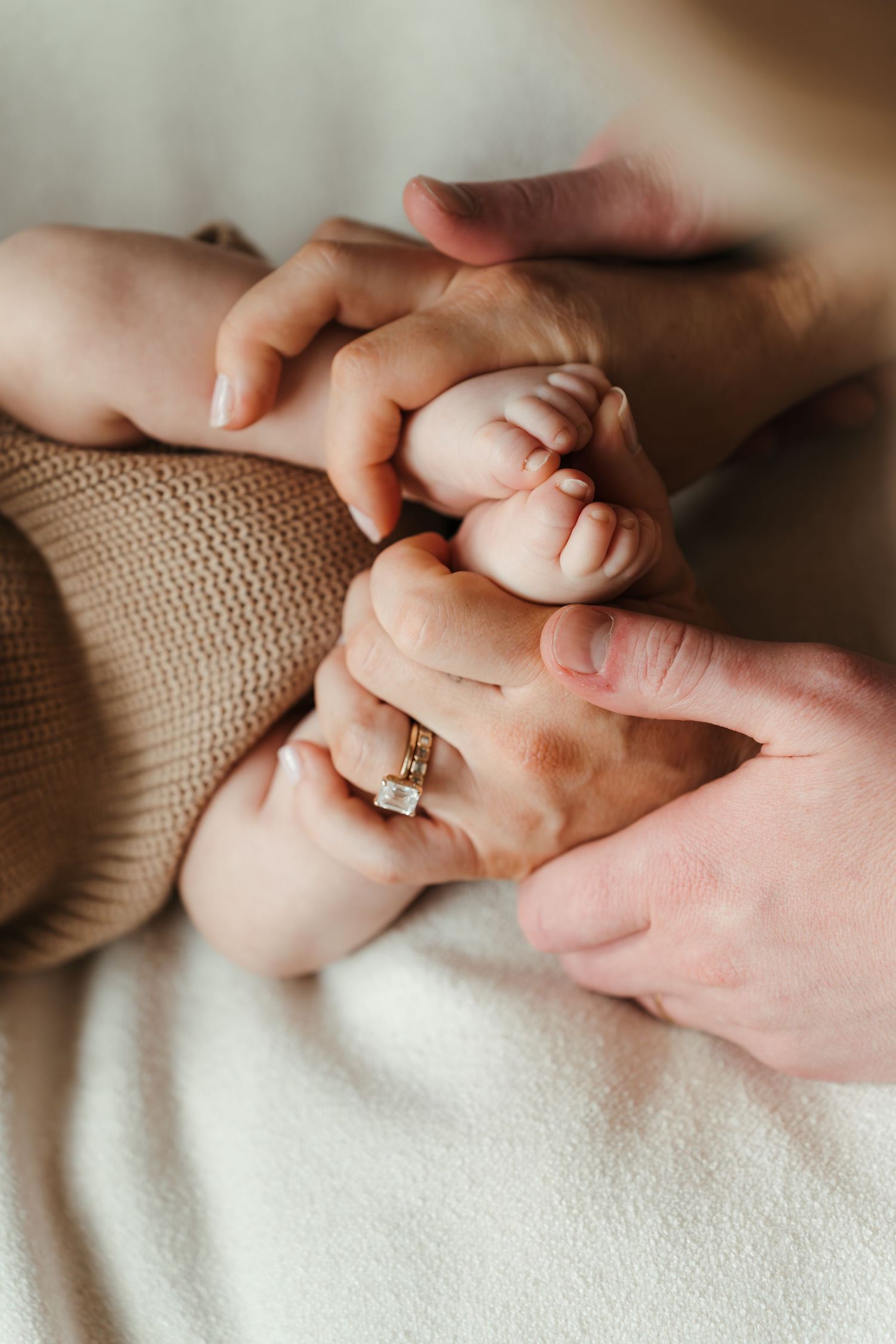Close-up of newborn baby’s tiny feet curled into his parents' hands in a Charlotte, NC lifestyle newborn session at home.