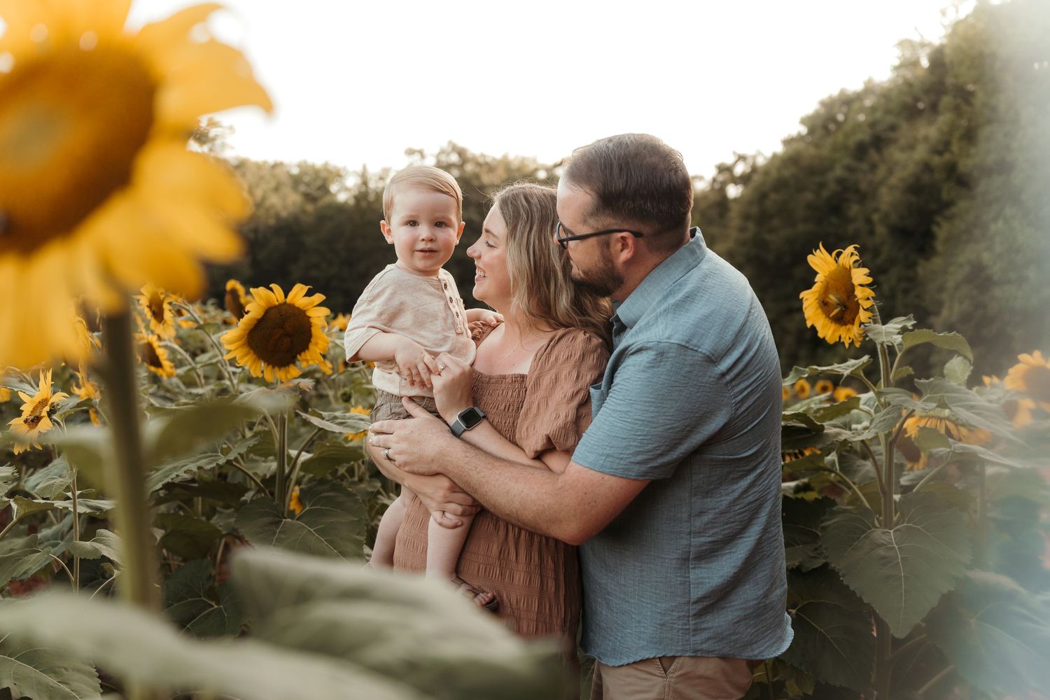 Family of three surrounded by sunflowers drenched in golden hour light during this outdoor session near Charlotte, NC.
