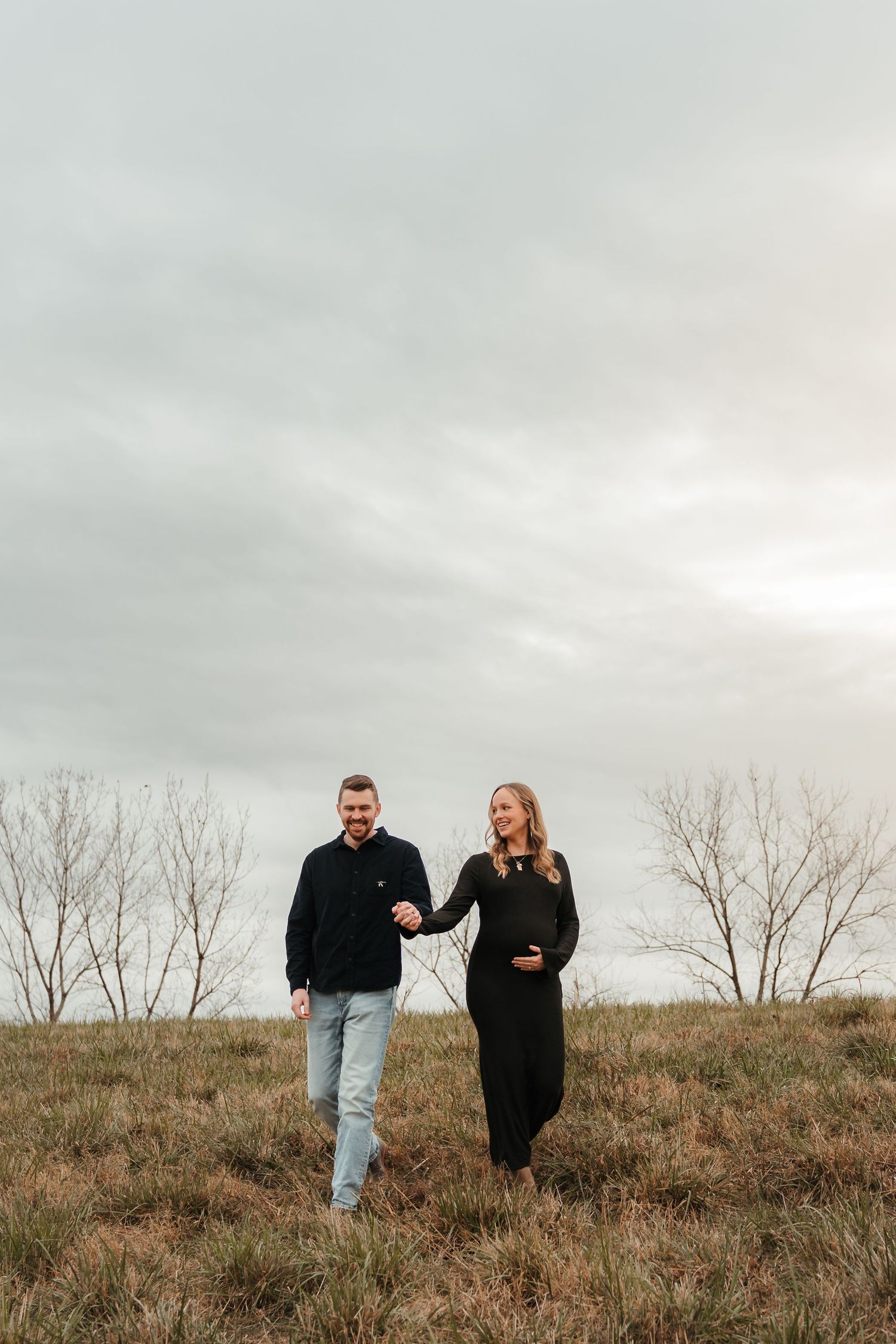 Expecting couple holding hands in an open field on an overcast day during an outdoor maternity session in Fort Mill, SC.