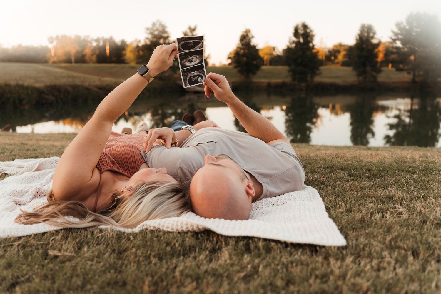 Expecting couple snuggling on a blanket in a Charlotte, NC park during a lifestyle maternity session.
