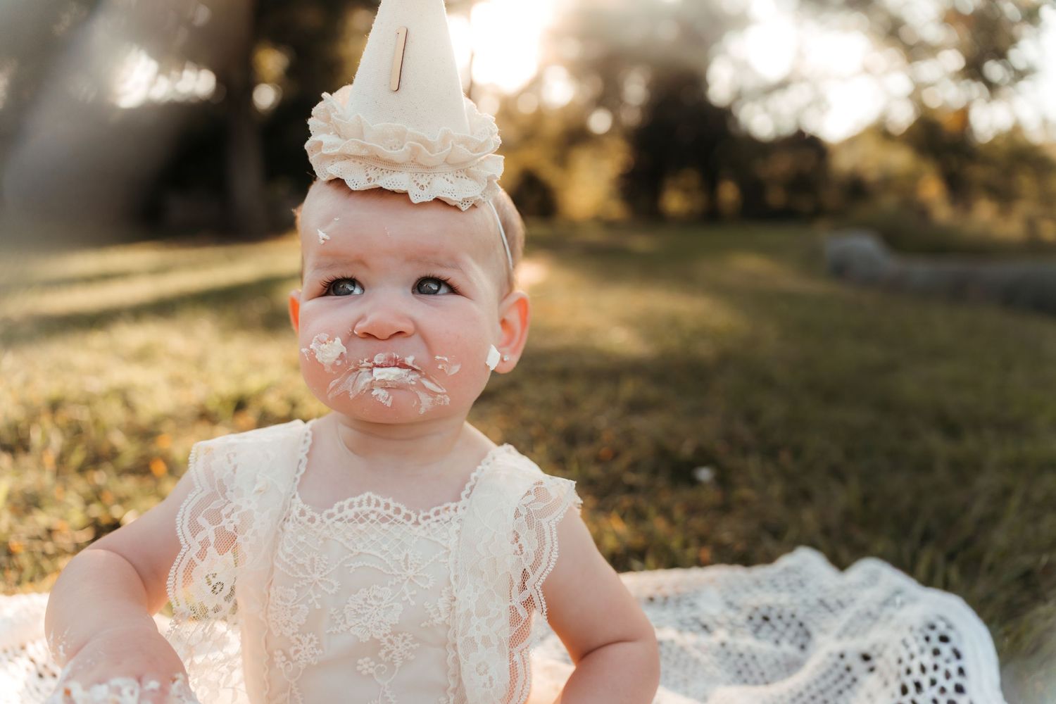 Child wearing birthday hat celebrating first birthday during a Charlotte, NC cake smash session outdoors.