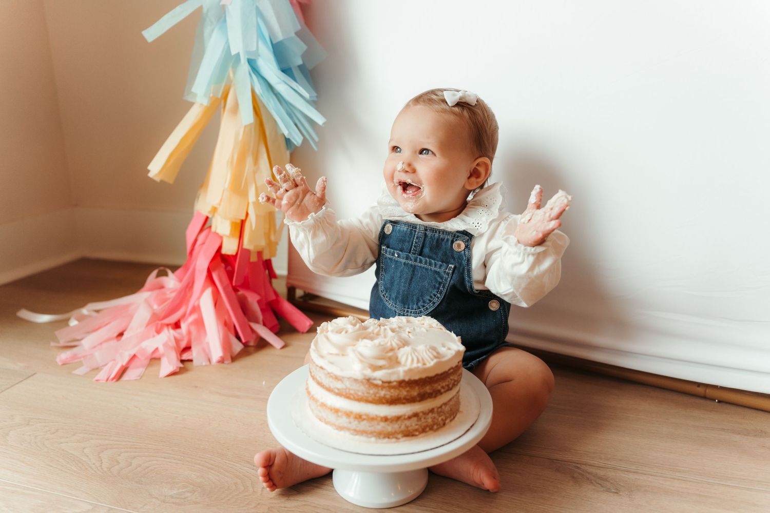 Child giggling while smashing cake in a Charlotte, NC lifestyle milestone session at home.
