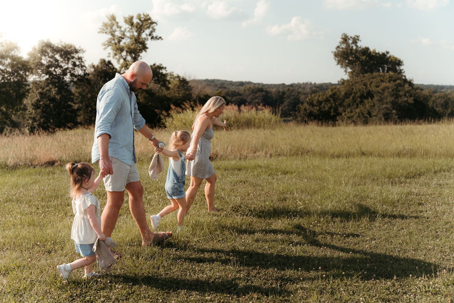 Family of four exploring a field, each child with their lovey, showcasing natural lifestyle photography in Charlotte, NC.