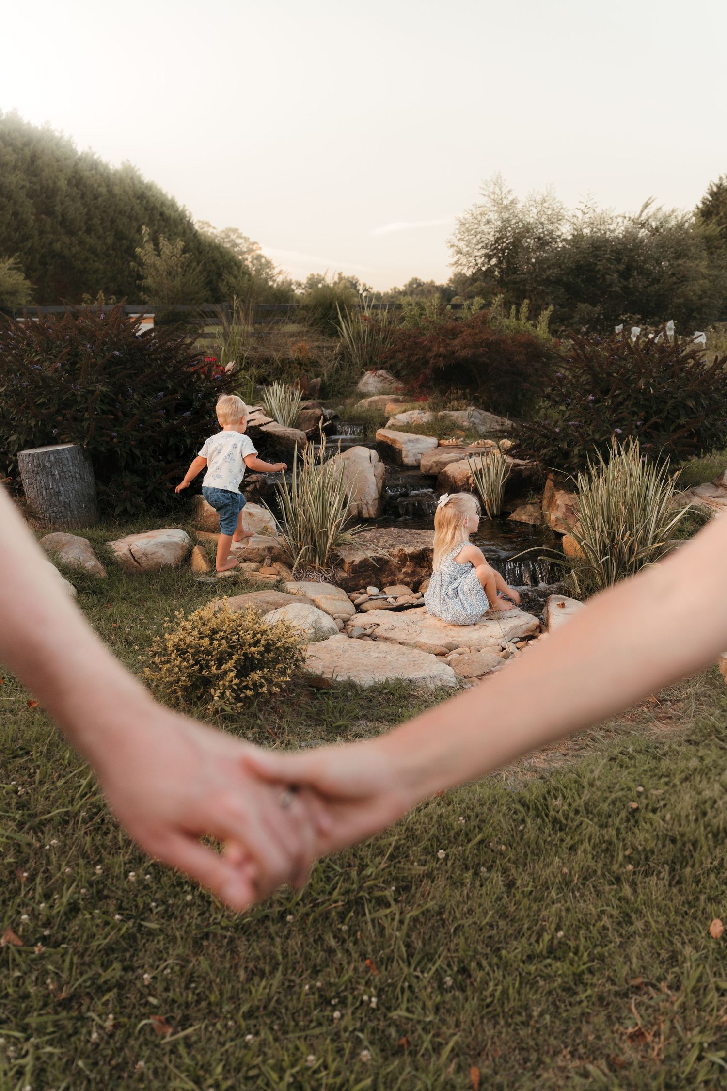 Siblings exploring a water feature during an outdoor lifestyle family session at Five Blossoms Farm located in Clover, SC.