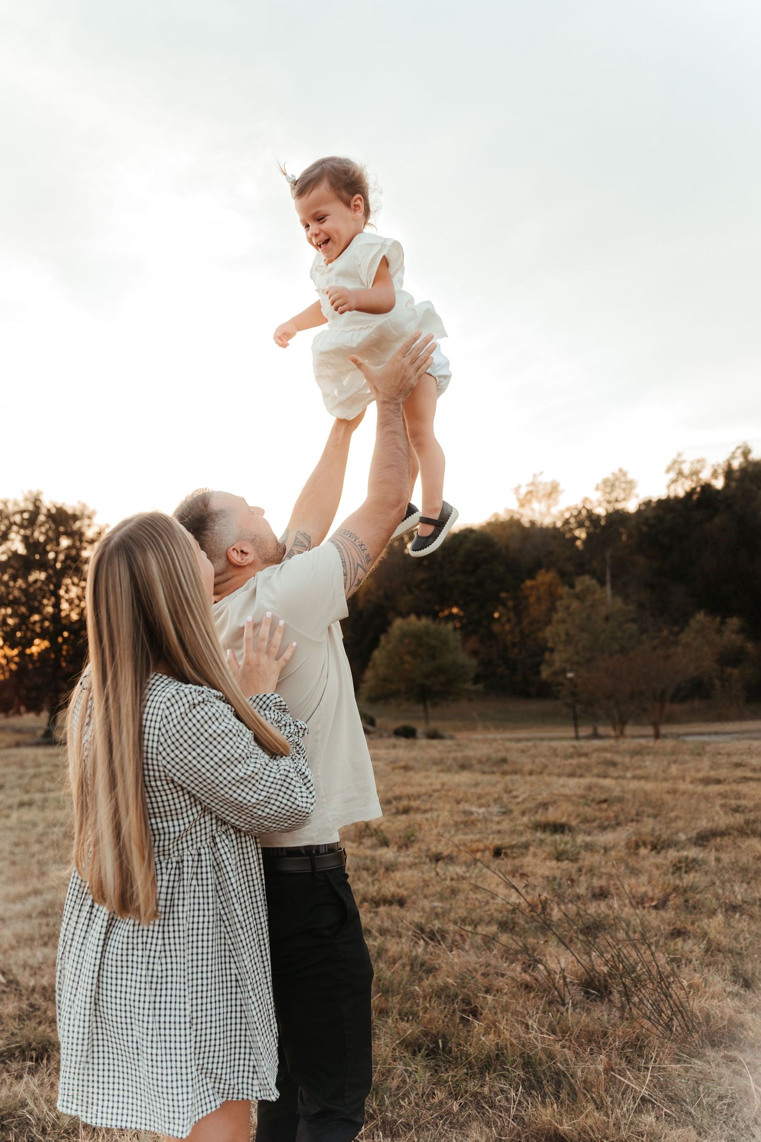 Little girl being tossed up in the air by her mother and father during a golden hour family photo session in Fort Mill, SC.