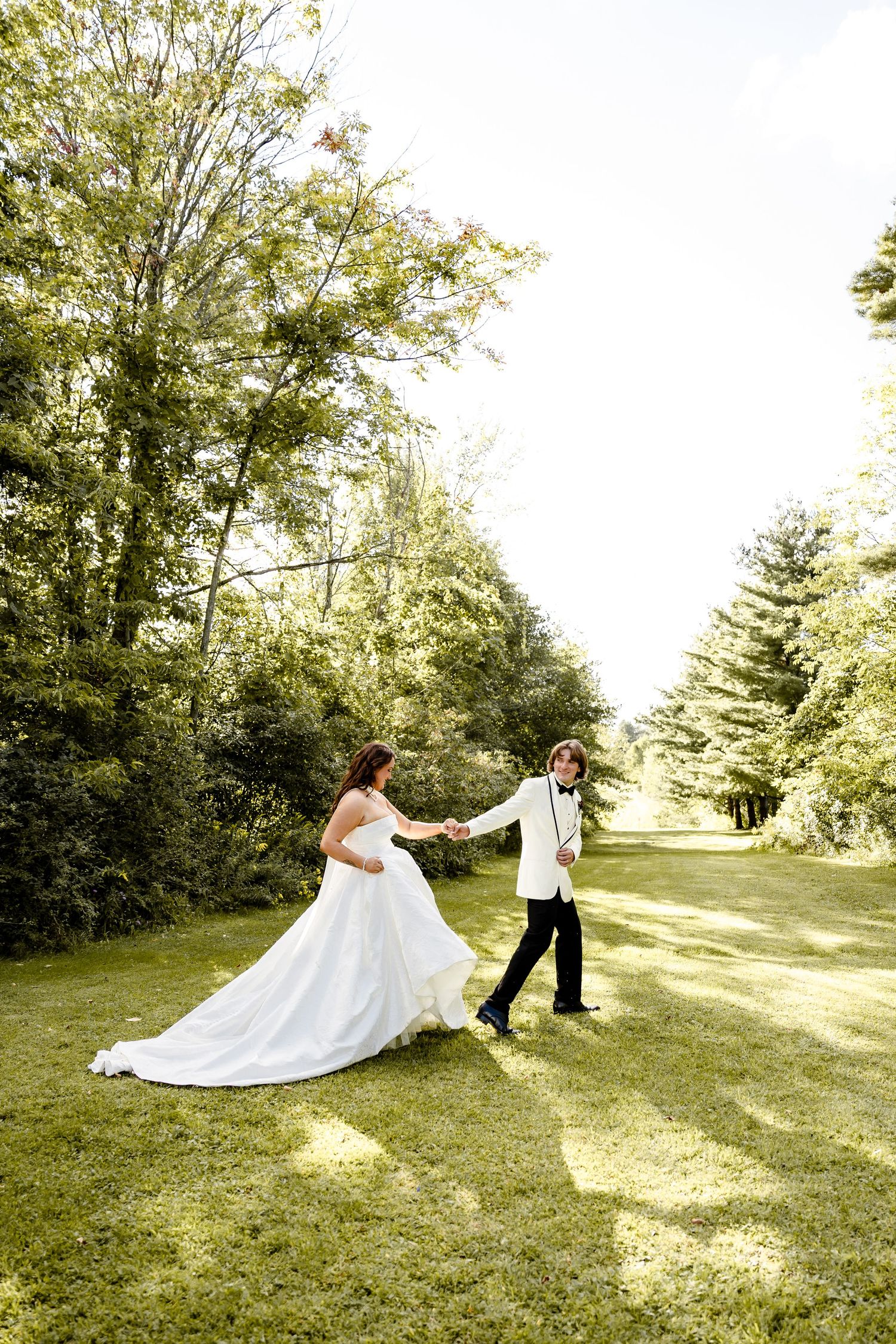 Bride and groom dancing on green lawn surrounded by lush trees on their wedding day.