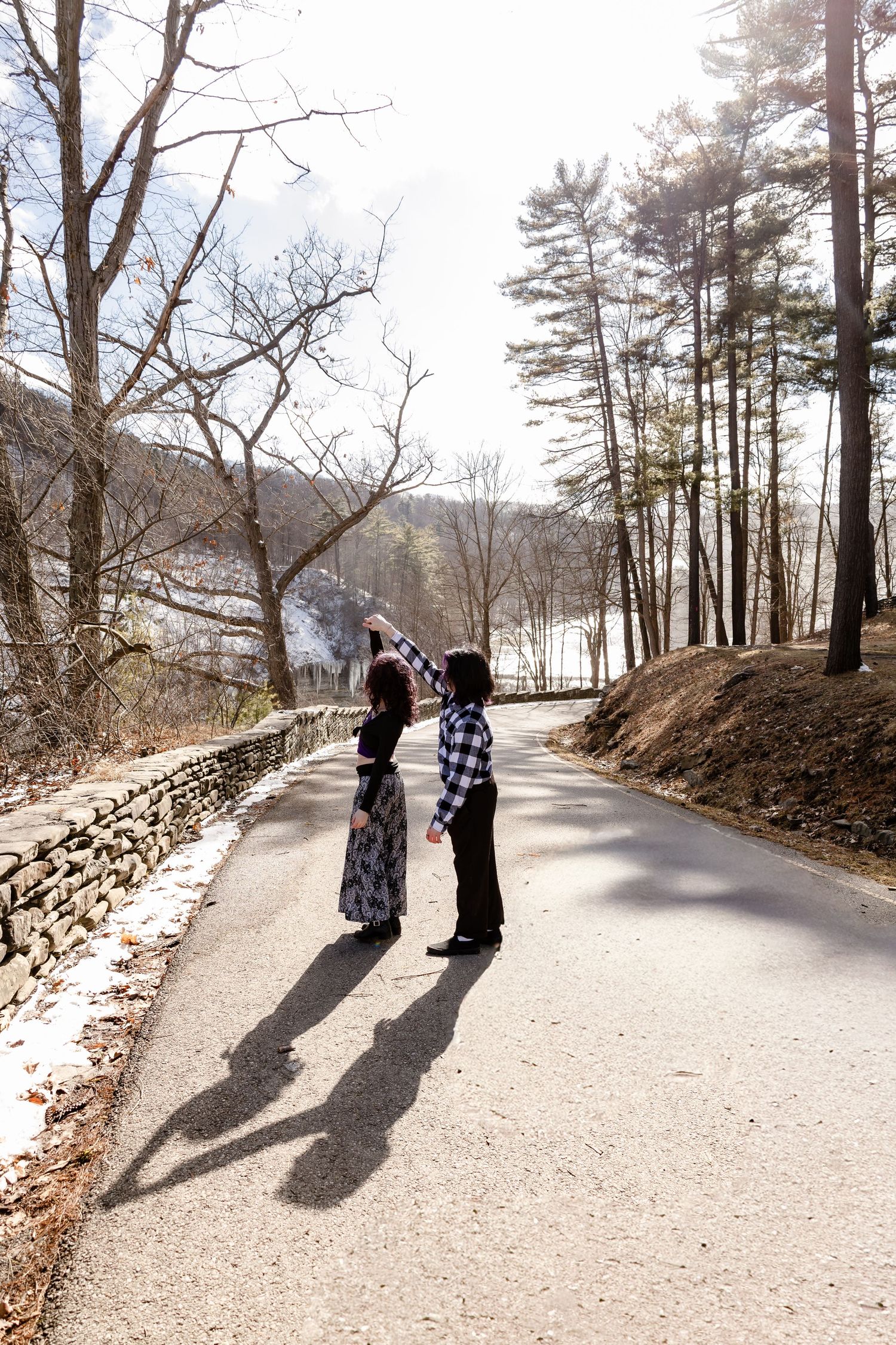 Couple dancing on a scenic road surrounded by bare trees and snow in a winter landscape.