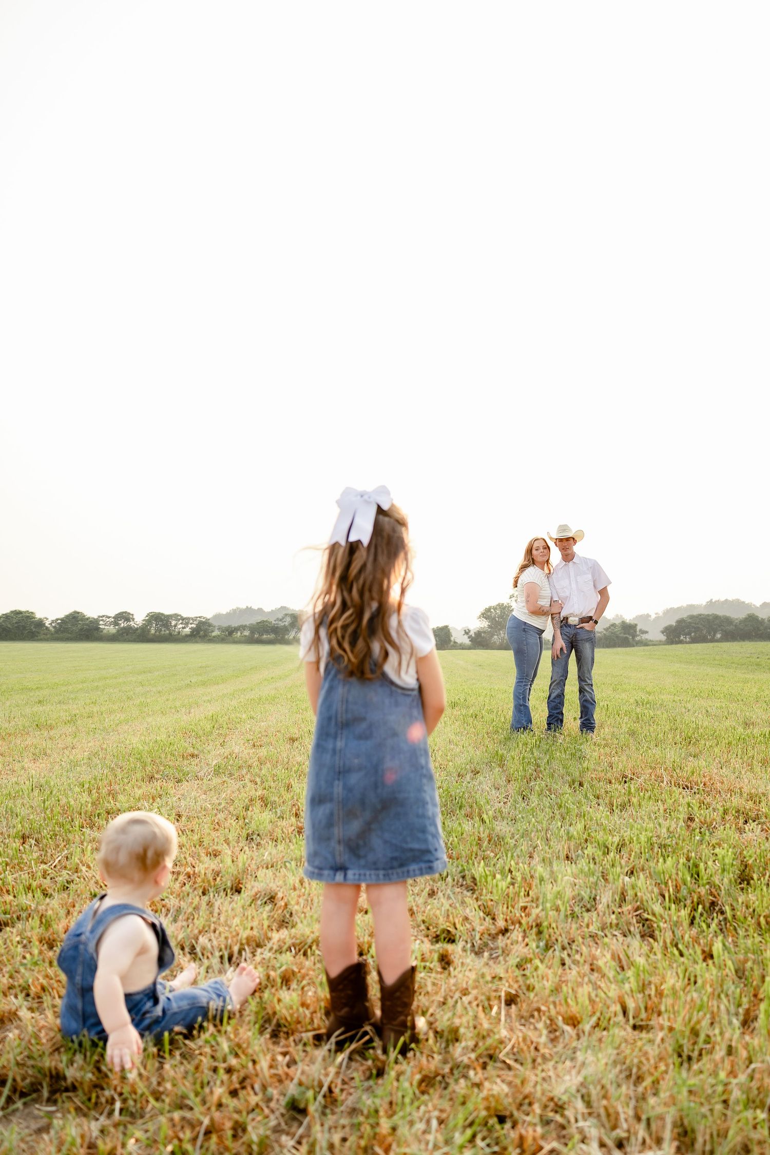 Family of four posing in a green field at golden hour, with children in denim and parents wearing cowboy hats.