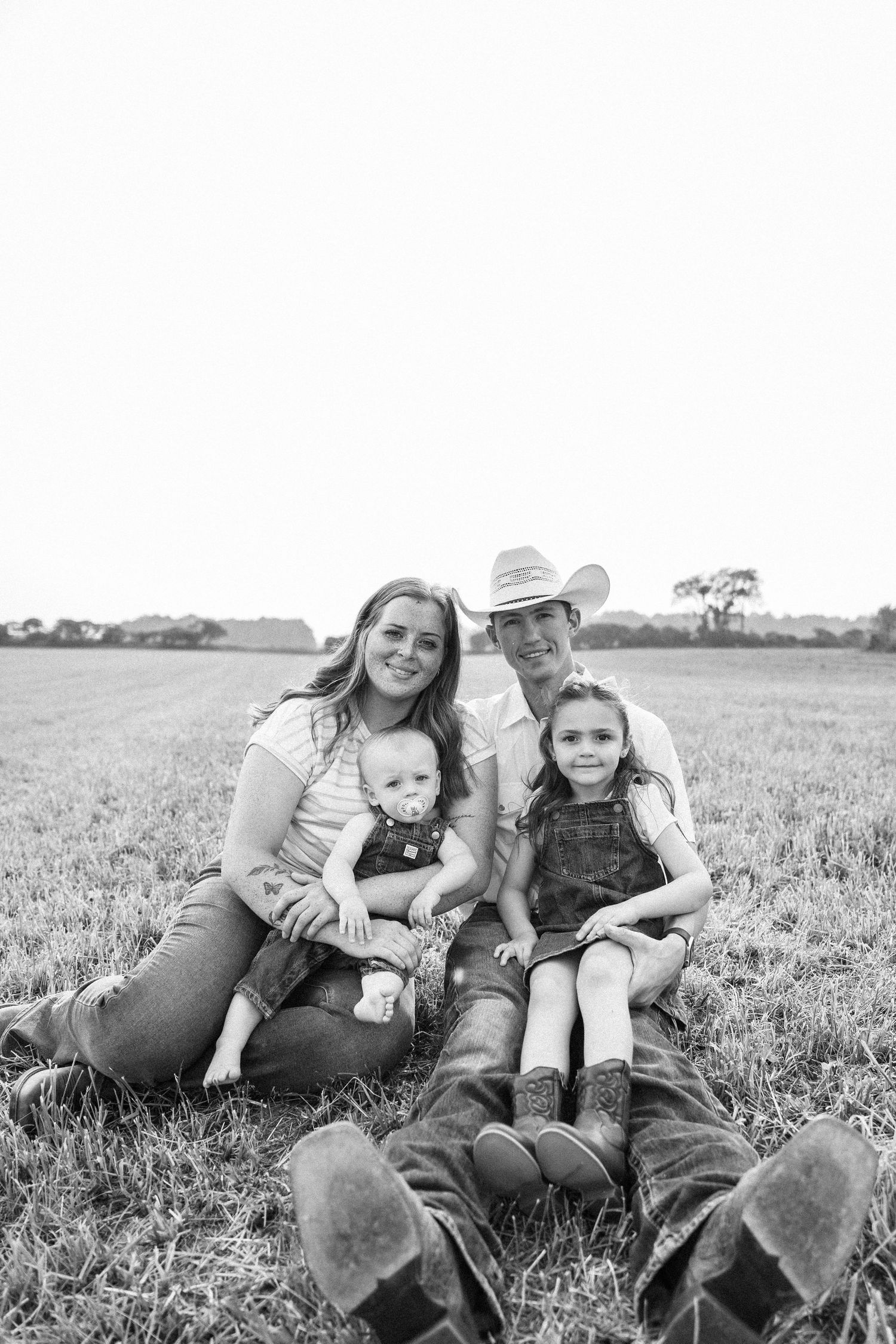Black and white family portrait of parents with baby and young girl sitting in a grassy field.