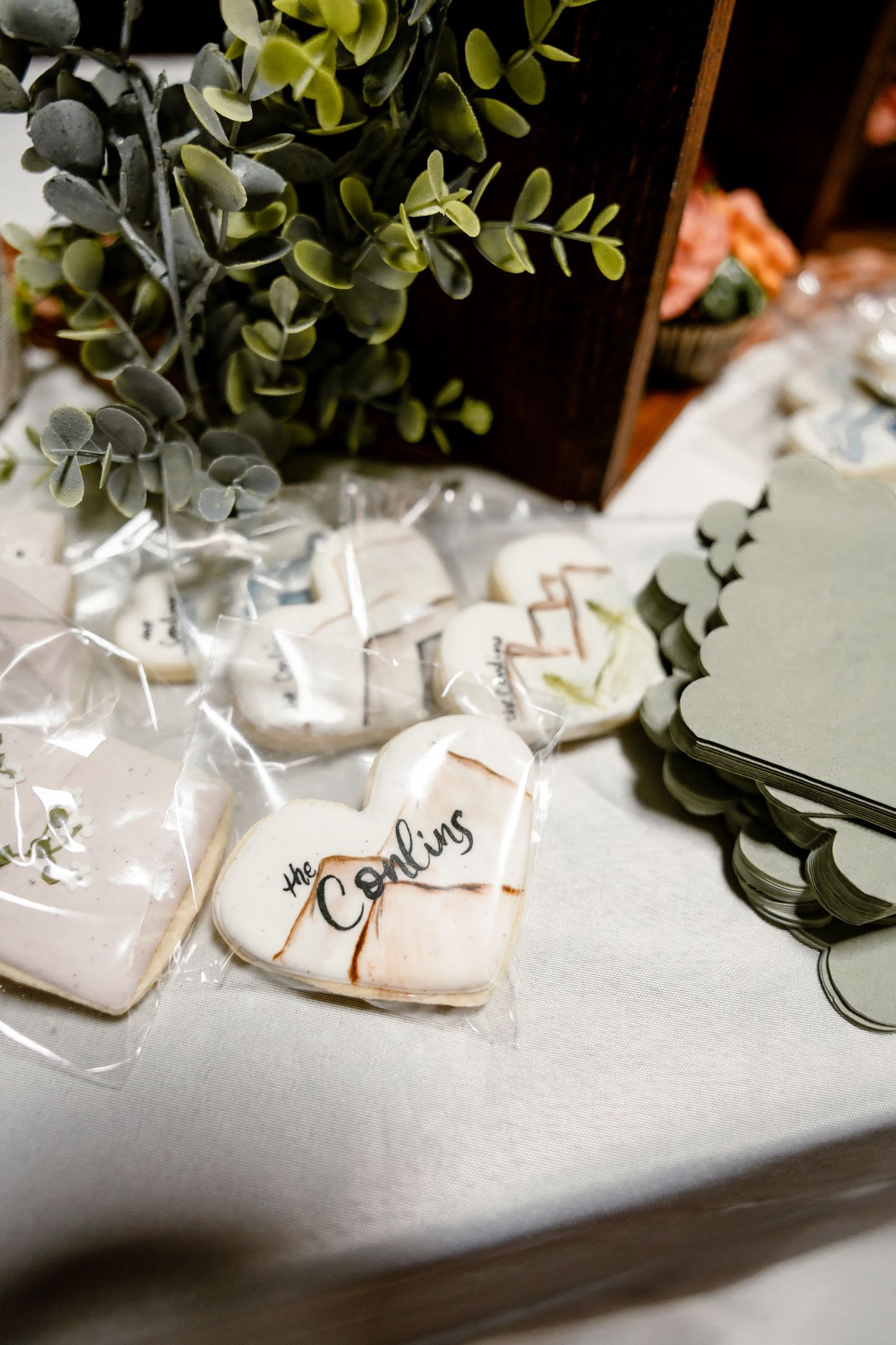 Heart-shaped wedding cookies with 'the Conlins' script icing displayed on a white table with greenery.