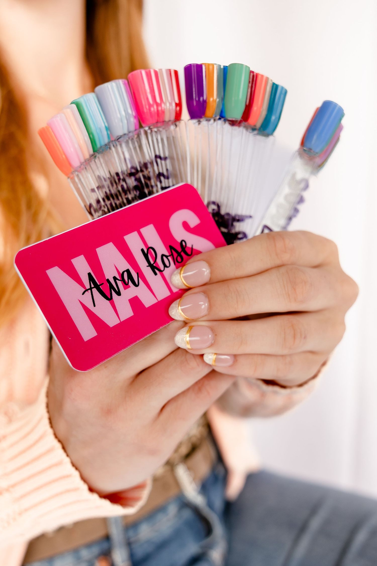 Person holding a pink Ava Rose Nails business card with colorful nail polish color swatches fan display.