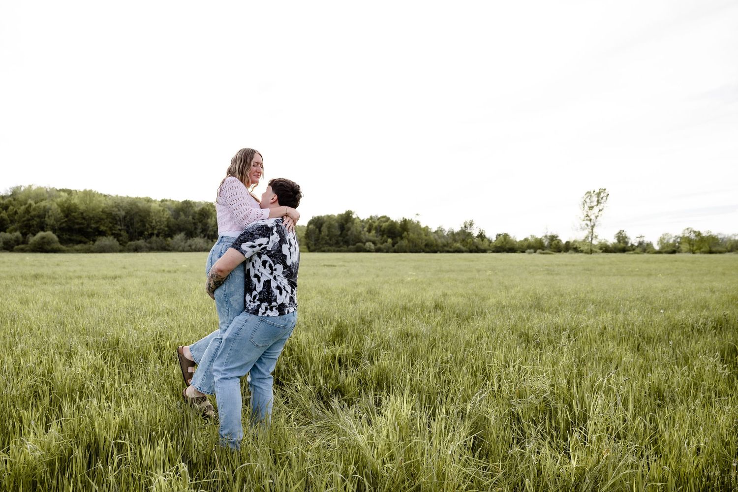 Couple sharing a joyful piggyback ride in a lush green field with trees in the background.