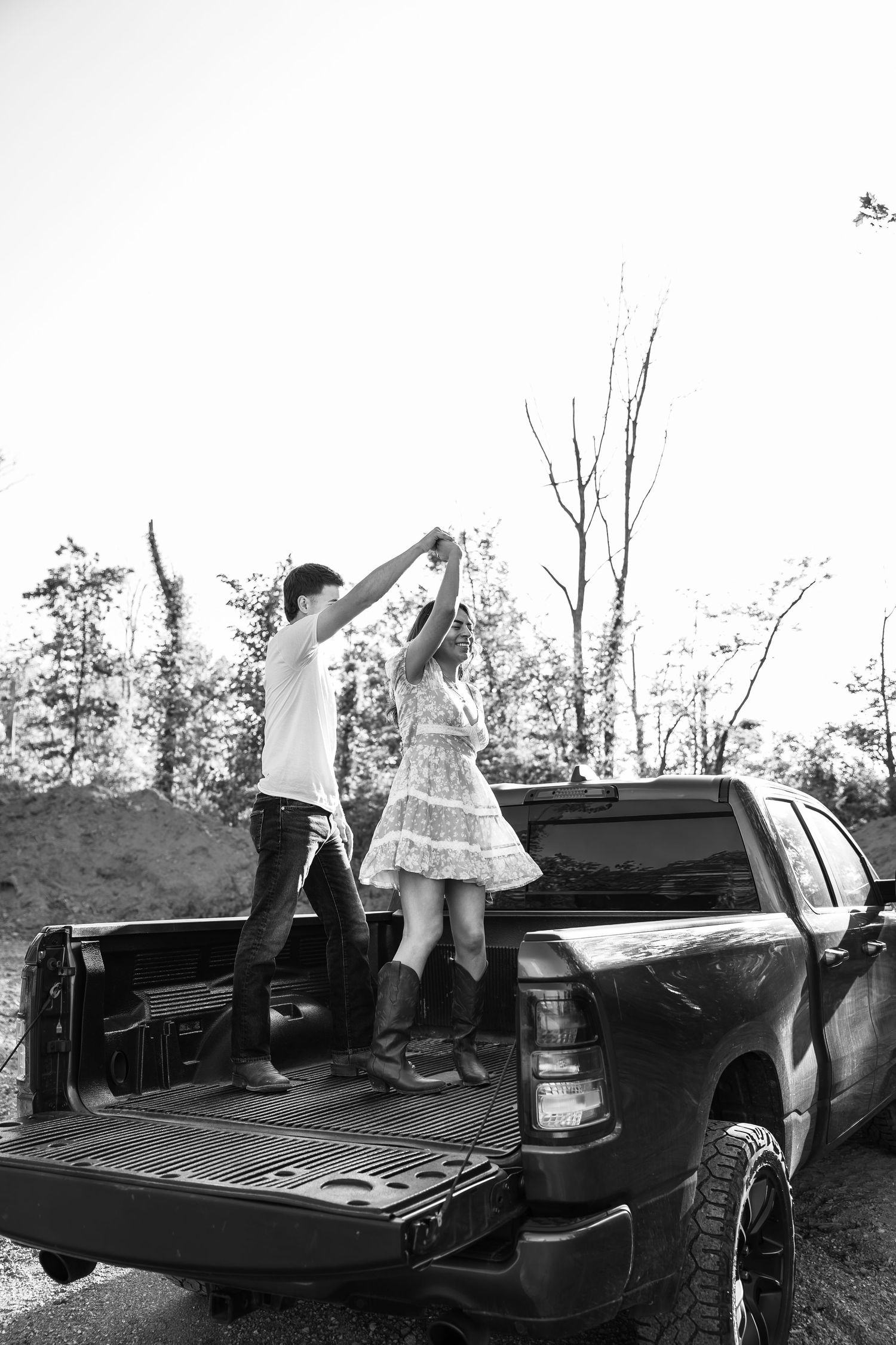 Couple dancing together in the bed of a pickup truck outdoors, black and white photo.