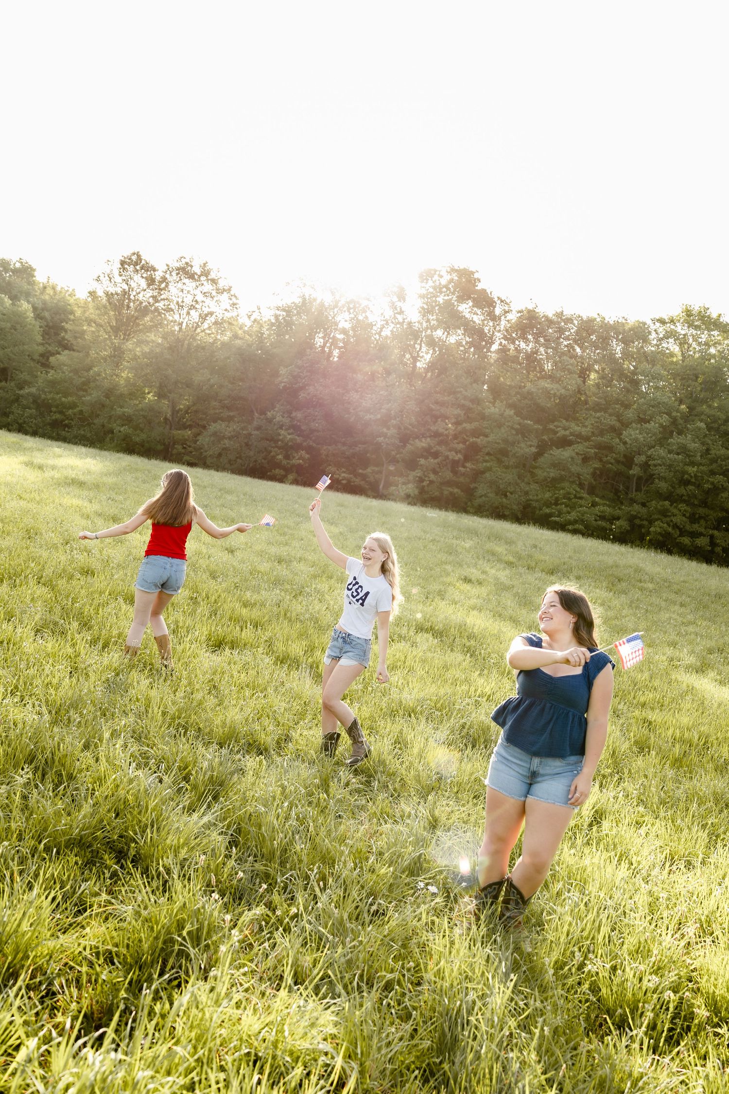 Three young women in denim shorts playing outdoors in a sunny green field, laughing and enjoying a summer day.