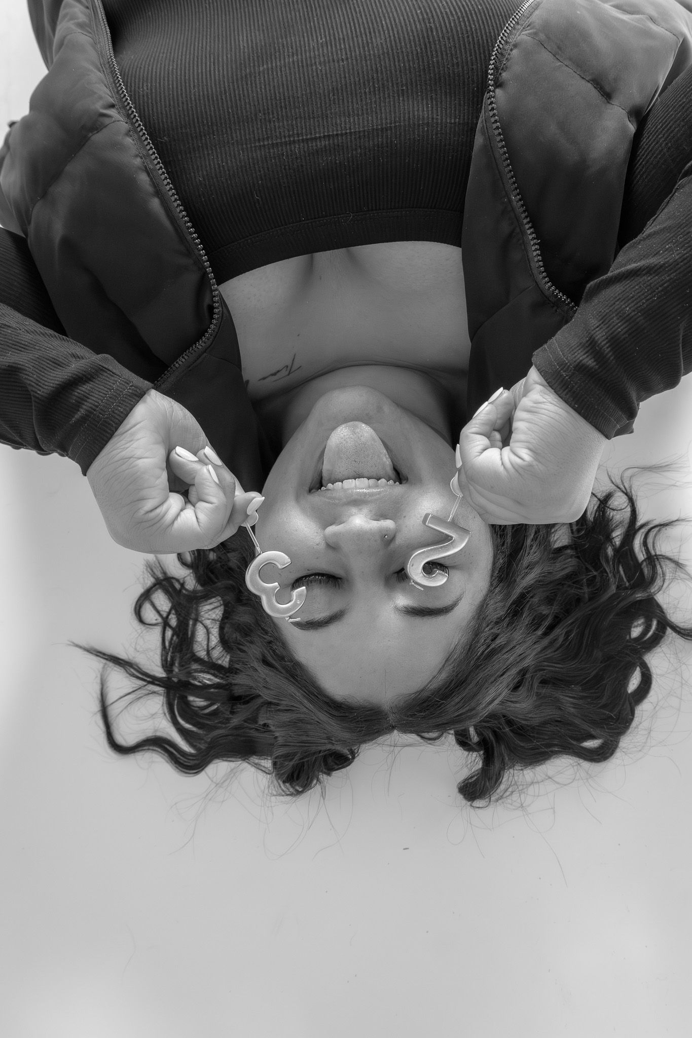 Black and white photo of a woman lying upside down, smiling, holding puzzle pieces near her face.