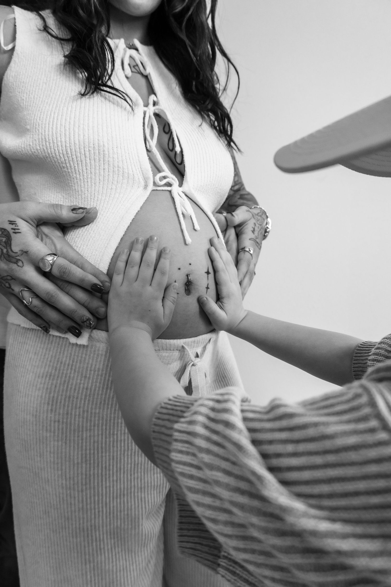 Black and white photo of multiple hands touching a pregnant woman's bare baby bump, celebrating new life.
