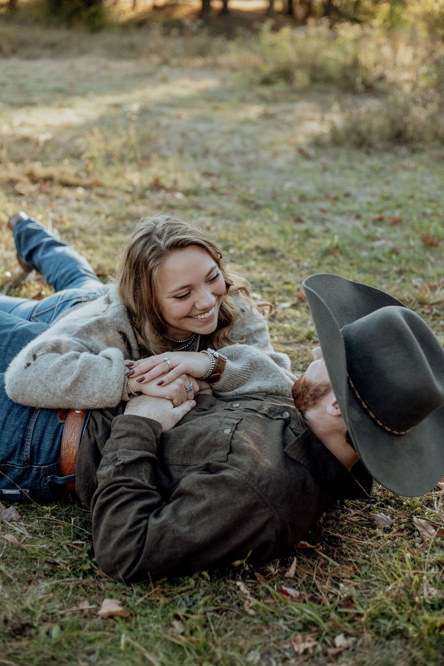 A couple lying on grass together in autumn, sharing intimate moments in casual outdoor attire.