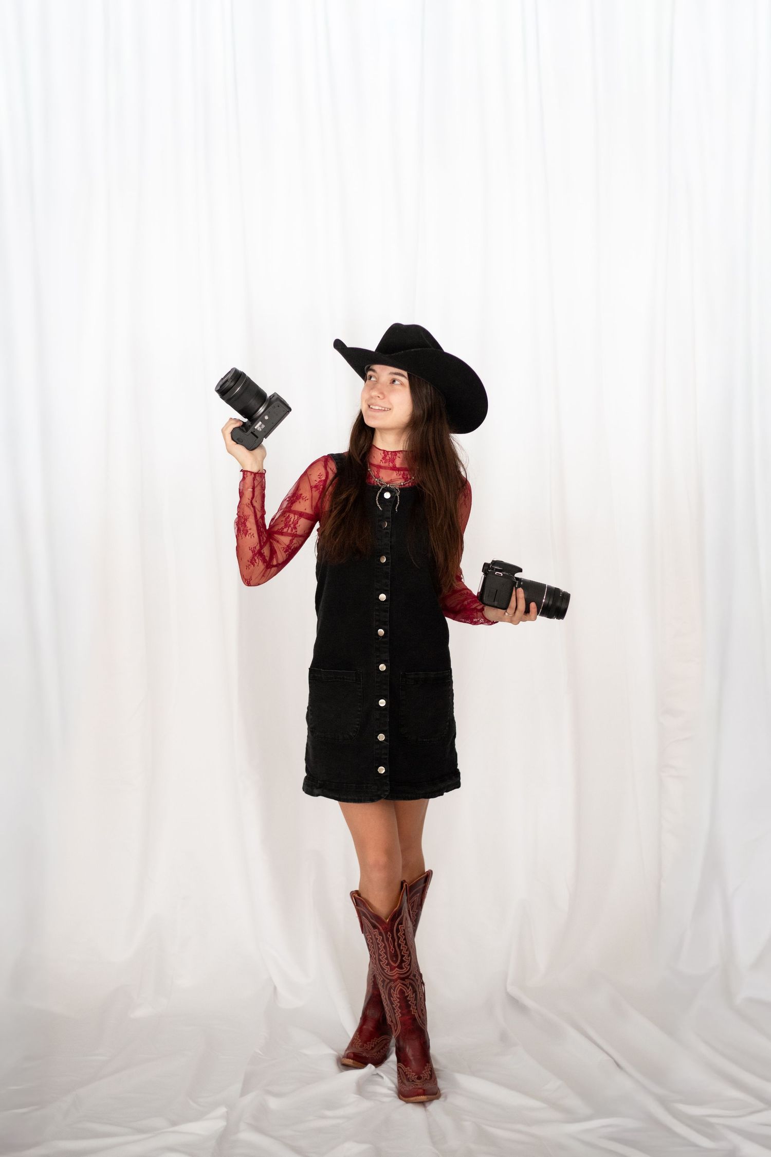 Person in black vest and cowboy boots holding camera equipment in studio setting.