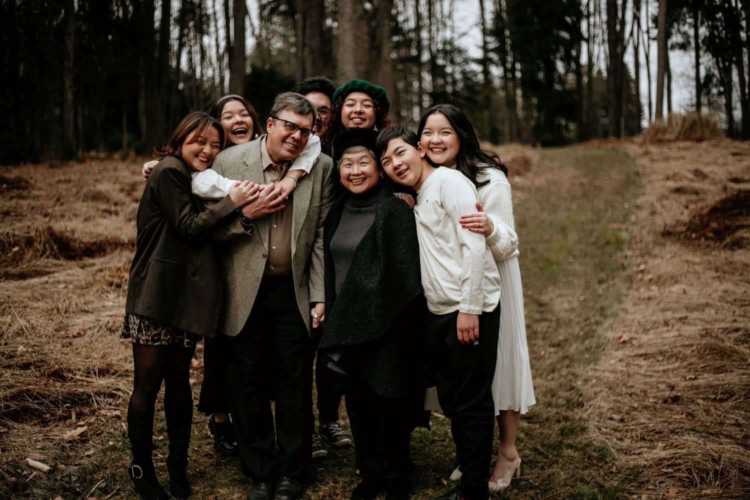 Group wedding photo with family members in casual winter attire against forest backdrop.