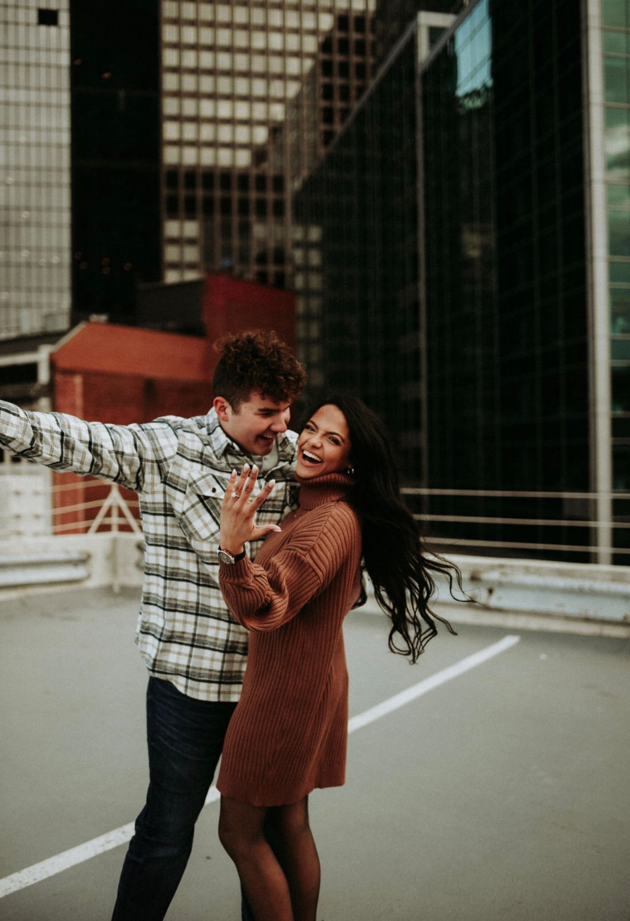 Happy couple celebrating engagement on urban rooftop.