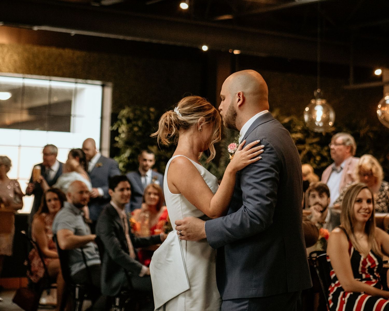 Wedding reception celebration with guests dancing and embracing on dimly lit dance floor.