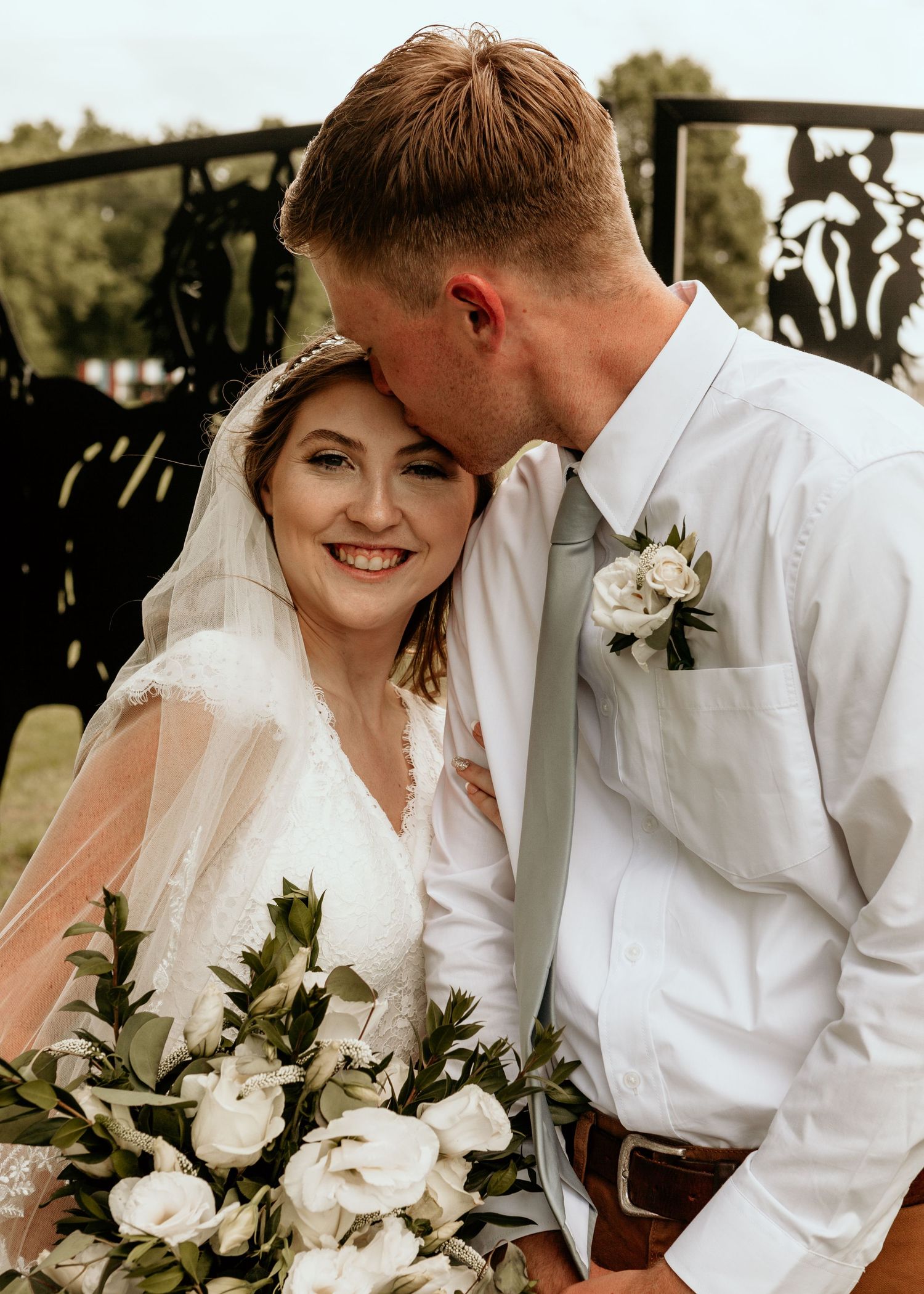 Romantic wedding portraits with white roses and greenery bouquet against rustic backdrop.