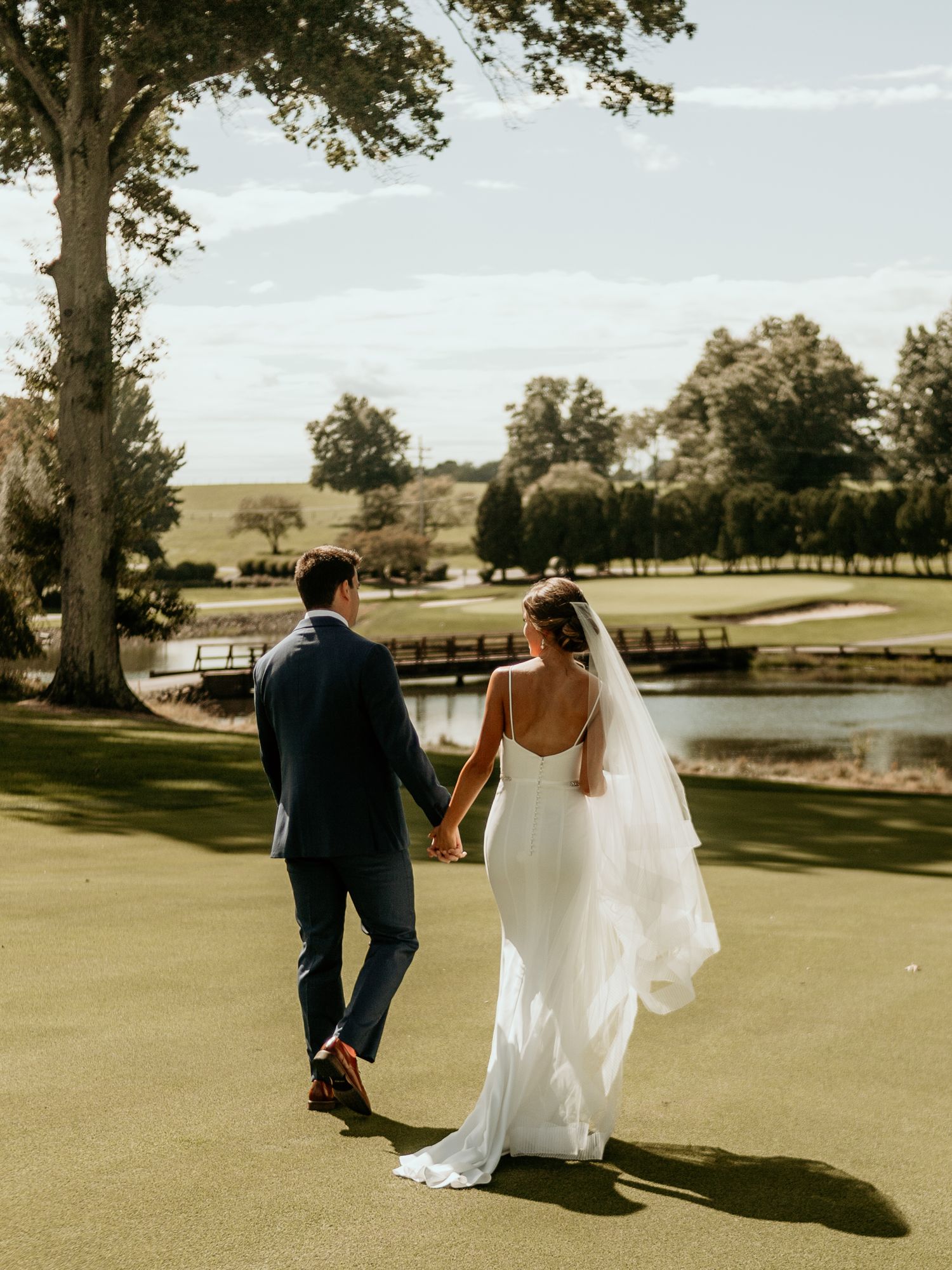 Newlyweds walk hand in hand on sunny golf course.