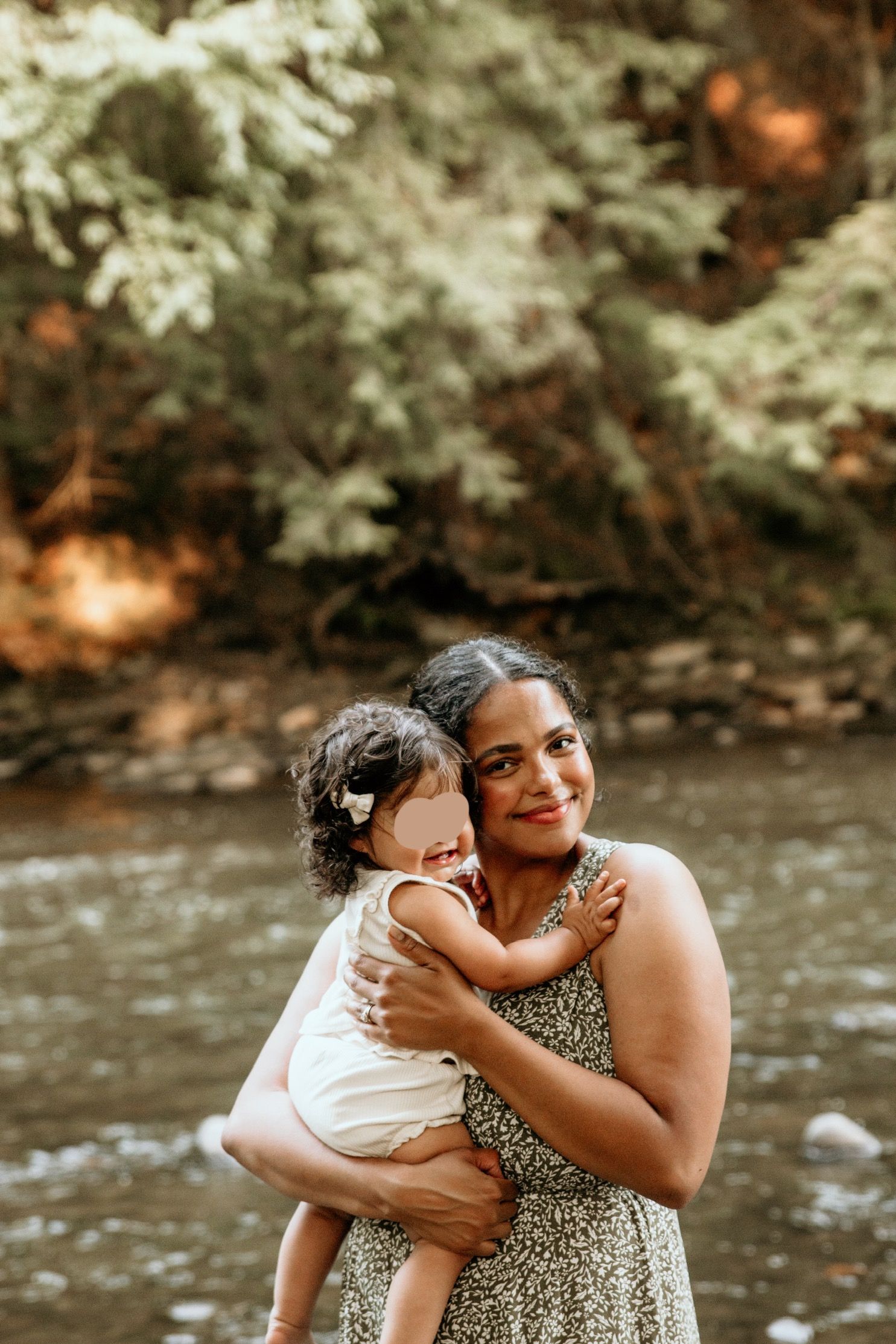 Mother and child share joyful moment by stream in nature setting.