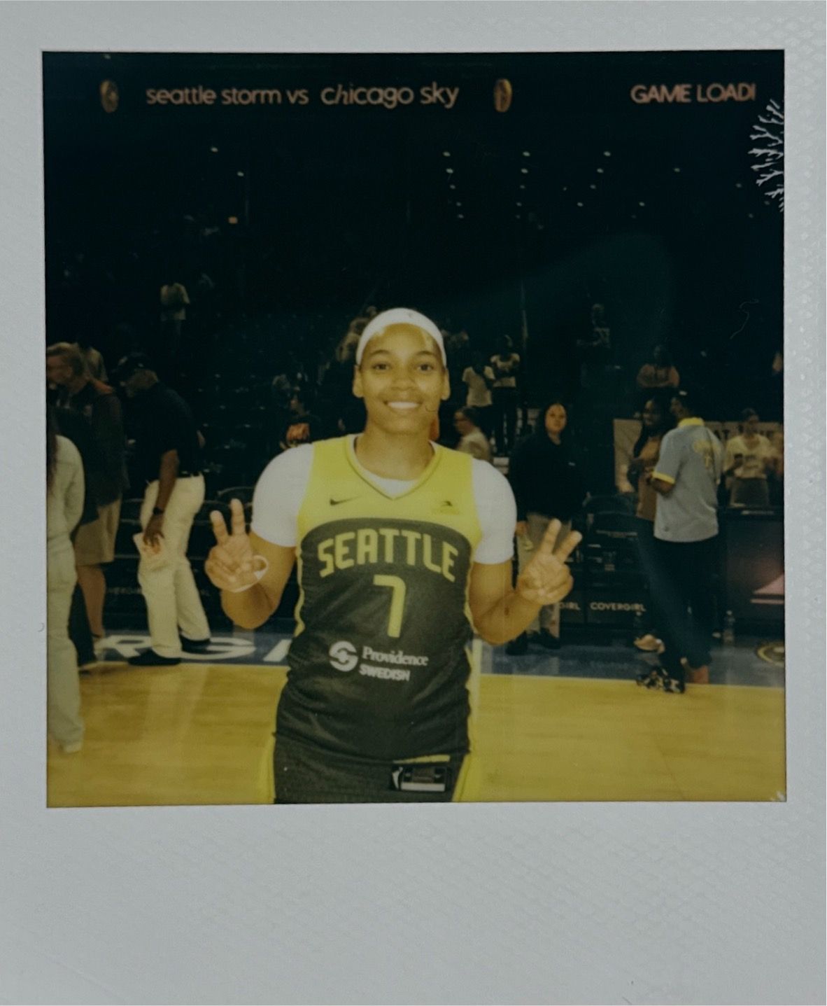 Basketball player in Seattle Storm uniform smiling on court during warmups.