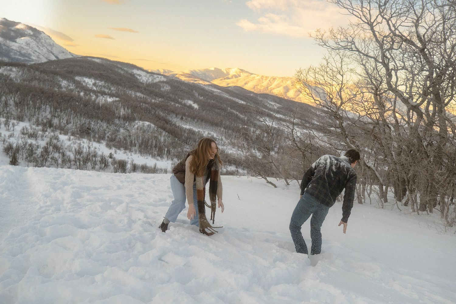 a couple having a snowball fight on top of a mountain in Utah, laughing, she had just thrown a snowball at him
