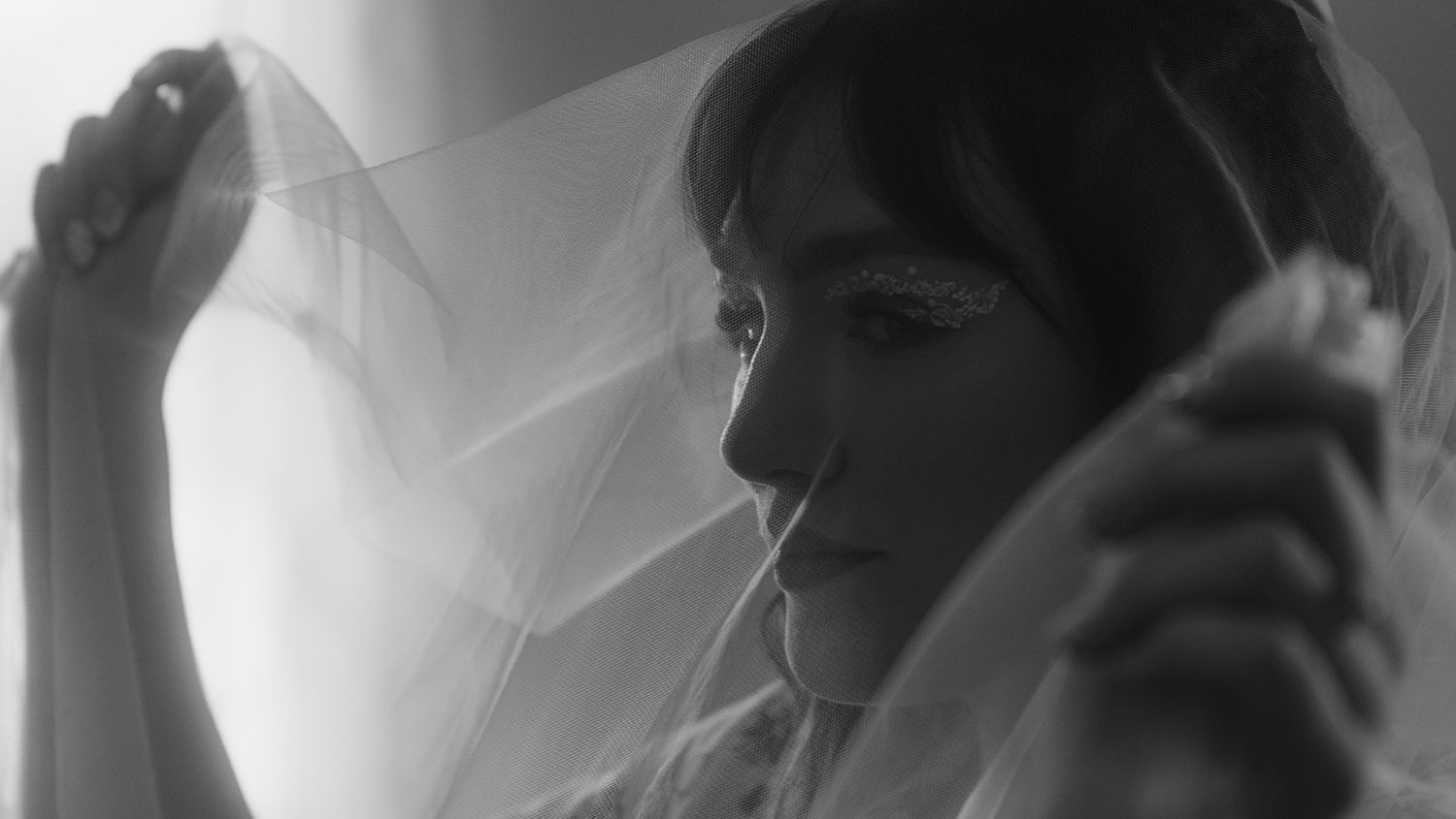 a bride holding her veil over her face near a window black and white, cinematic