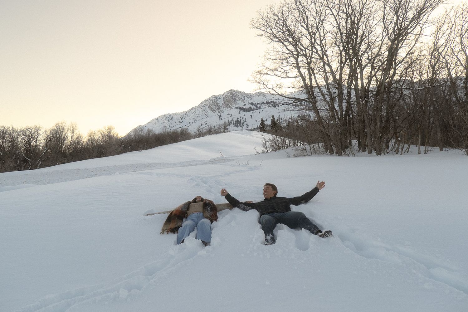 a couple doing snow angels in the mountains at sunset