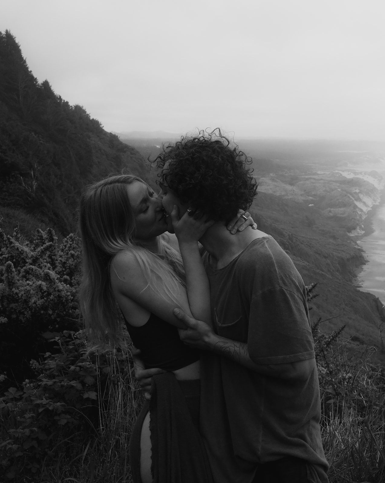 a couple shares a kiss cliffside in Oregon on the coast, black and white, passionate.