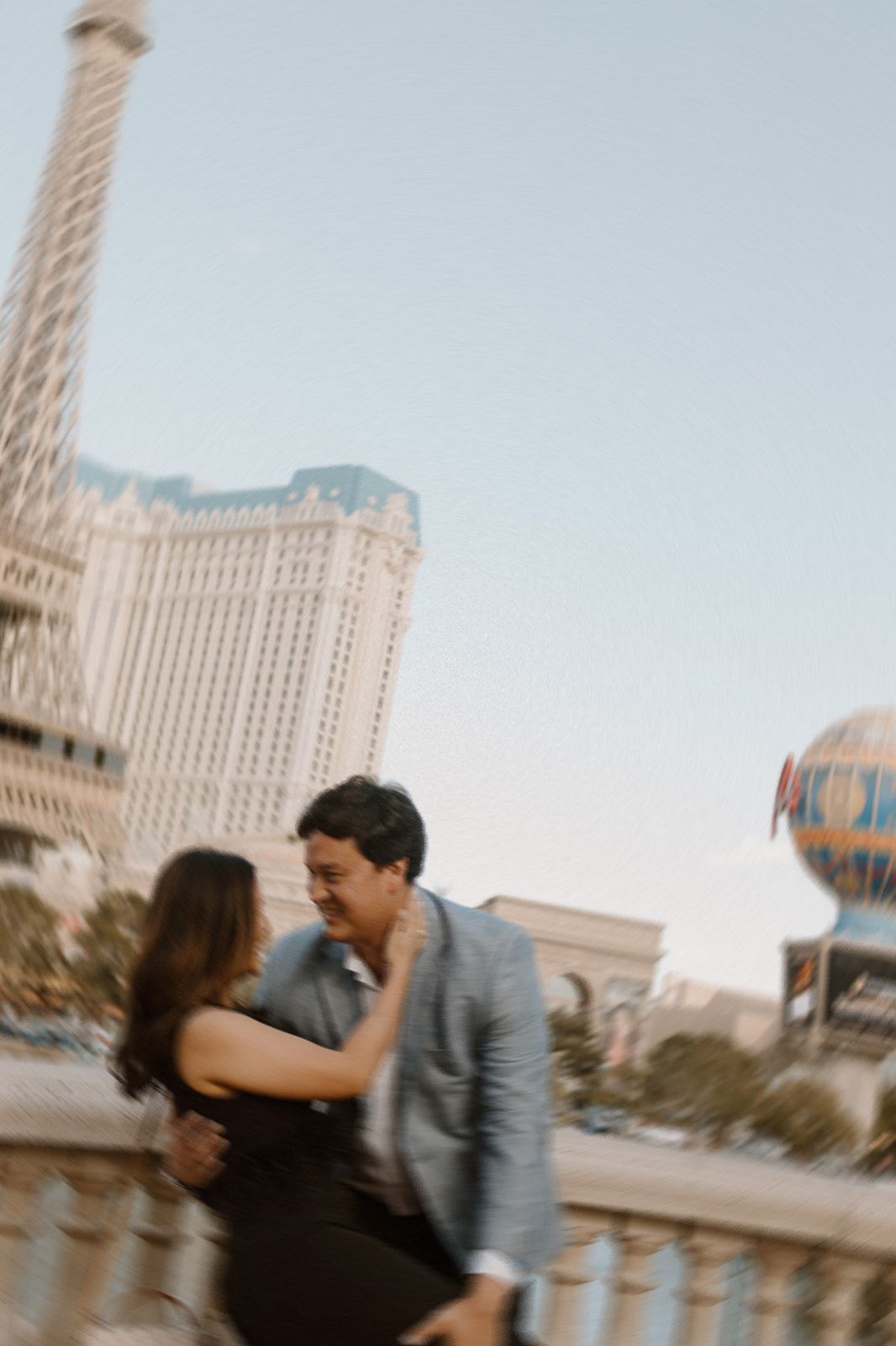 a couple leaning into the fountains outside the bellagio in Las Vegas, blue skies, tall casinos, eiffel tower